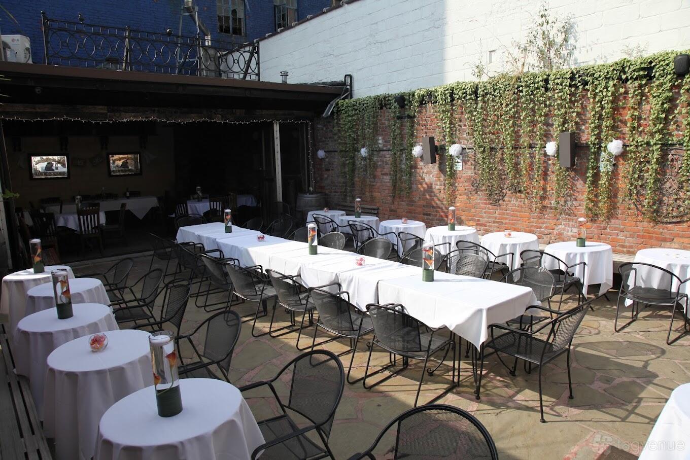 A garden venue with round tables covered in white linens and hanging greenery on brick walls at LIC Weddings.