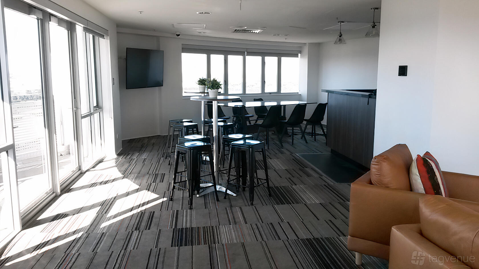 A hotel lounge with striped carpet, high tables and stools, large windows, and a small bar at Novotel Sydney Olympic Park Hotel.