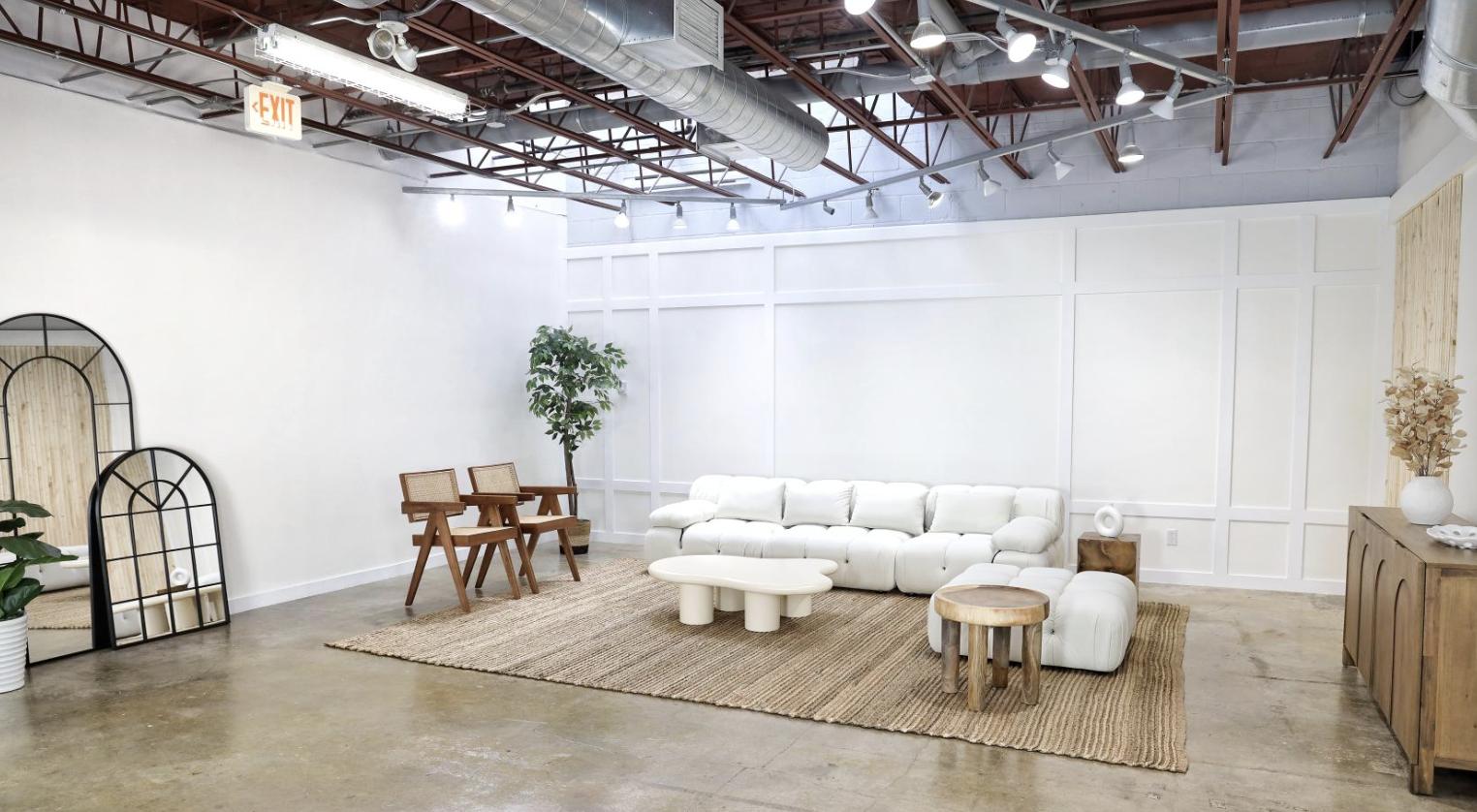 A photo studio with a white tufted sofa, wooden chairs, and exposed ductwork at Shvrk Studio Kensington.