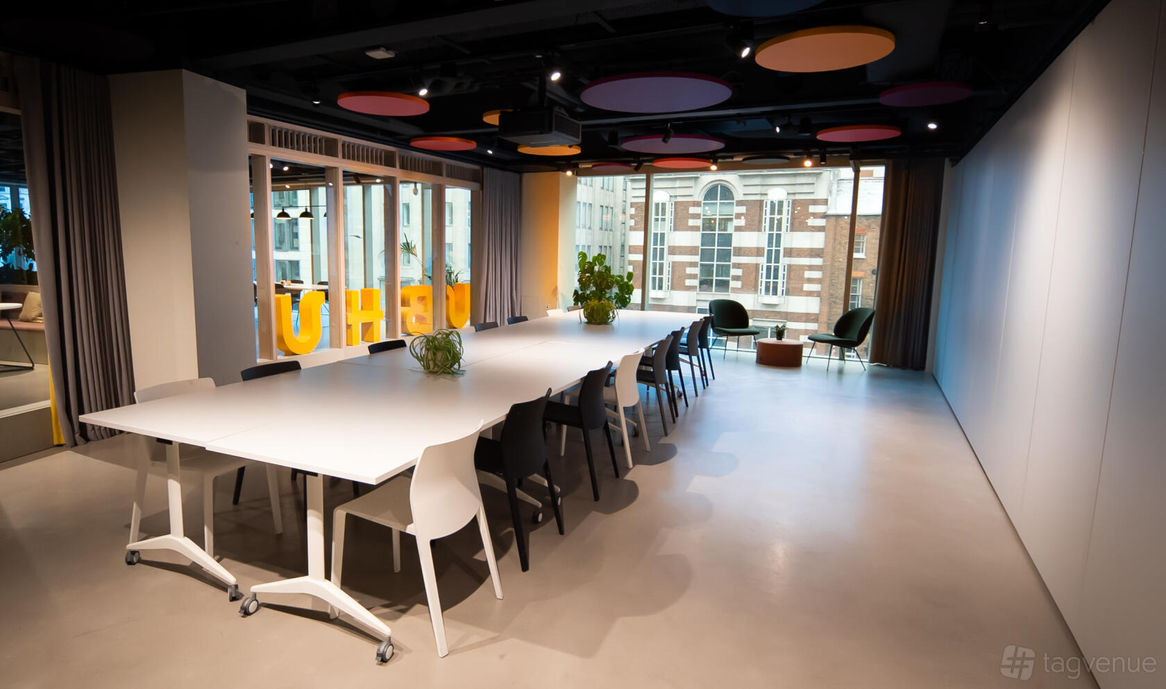 A boardroom with a long white table, modern chairs, potted plants, and large windows at HubHub 20 Farringdon Street.