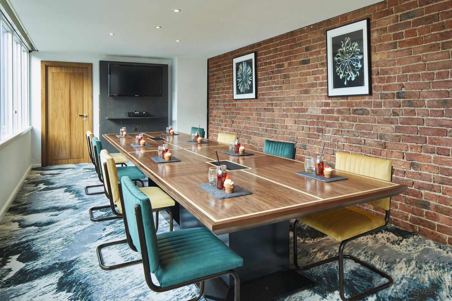 A hotel meeting room with exposed brick walls, large windows, and a long wooden table at Marriott Victoria & Albert Hotel.