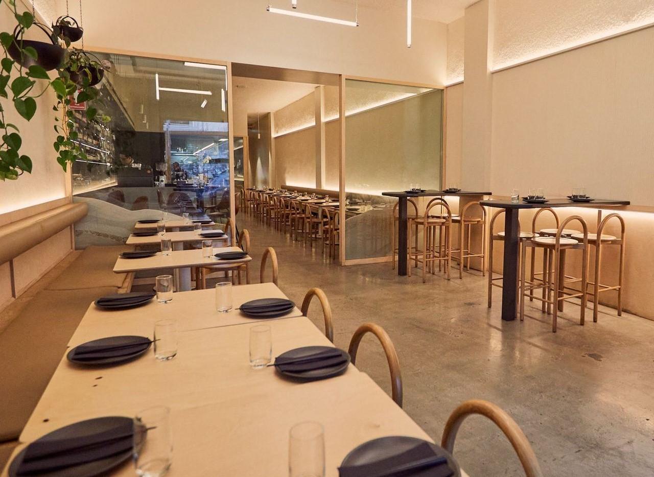 A restaurant with long wooden tables, minimalist chairs, and ambient lighting at Eazy Peazy.