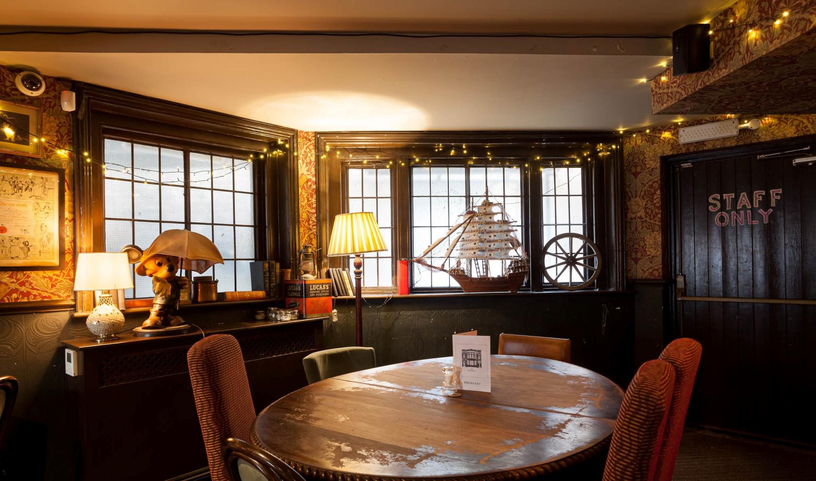 An event space in a pub with round wooden table, vintage lamps, and string lights at The Walrus