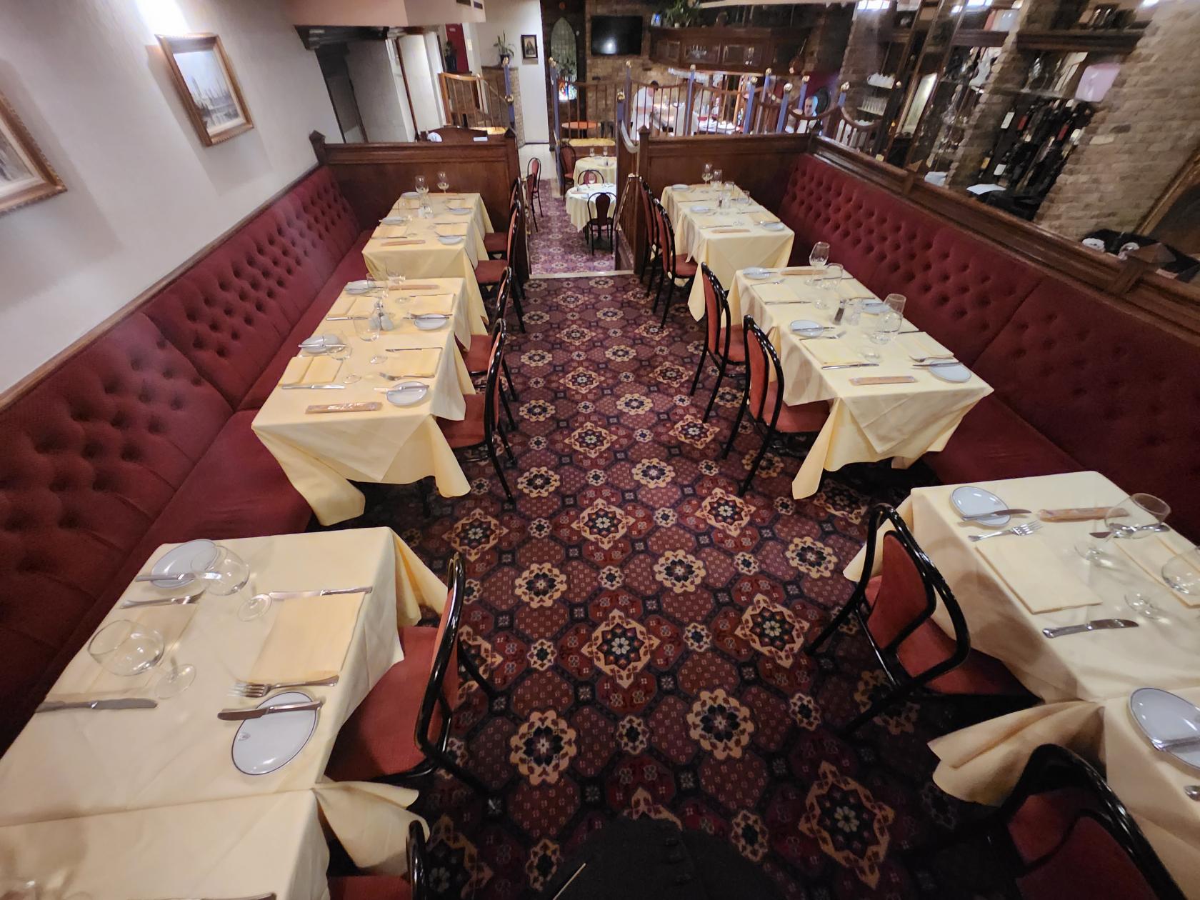 A restaurant dining area with red upholstered banquettes, patterned carpet, and tables set with cream linens at Bolton's.