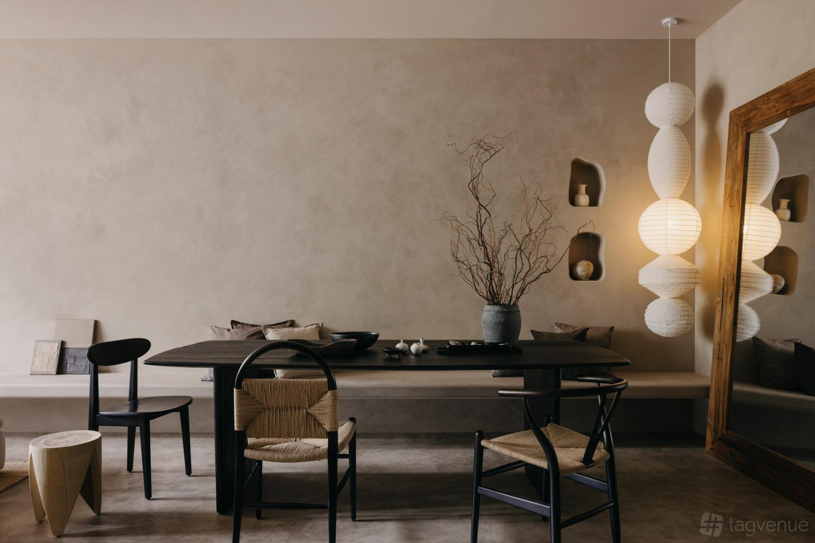 A lounge with a dark wooden table, mixed chairs, natural wall niches, and paper lantern lighting at Anthology.