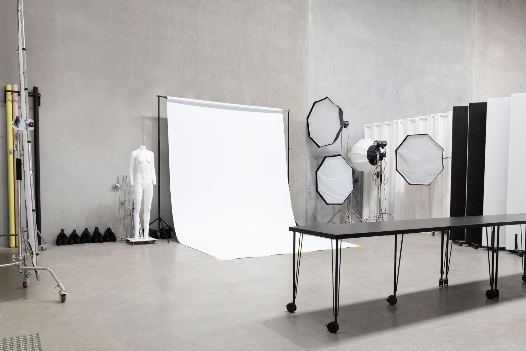 A photo studio with a white backdrop, lighting equipment, and a black table on wheels at Jem Studios.