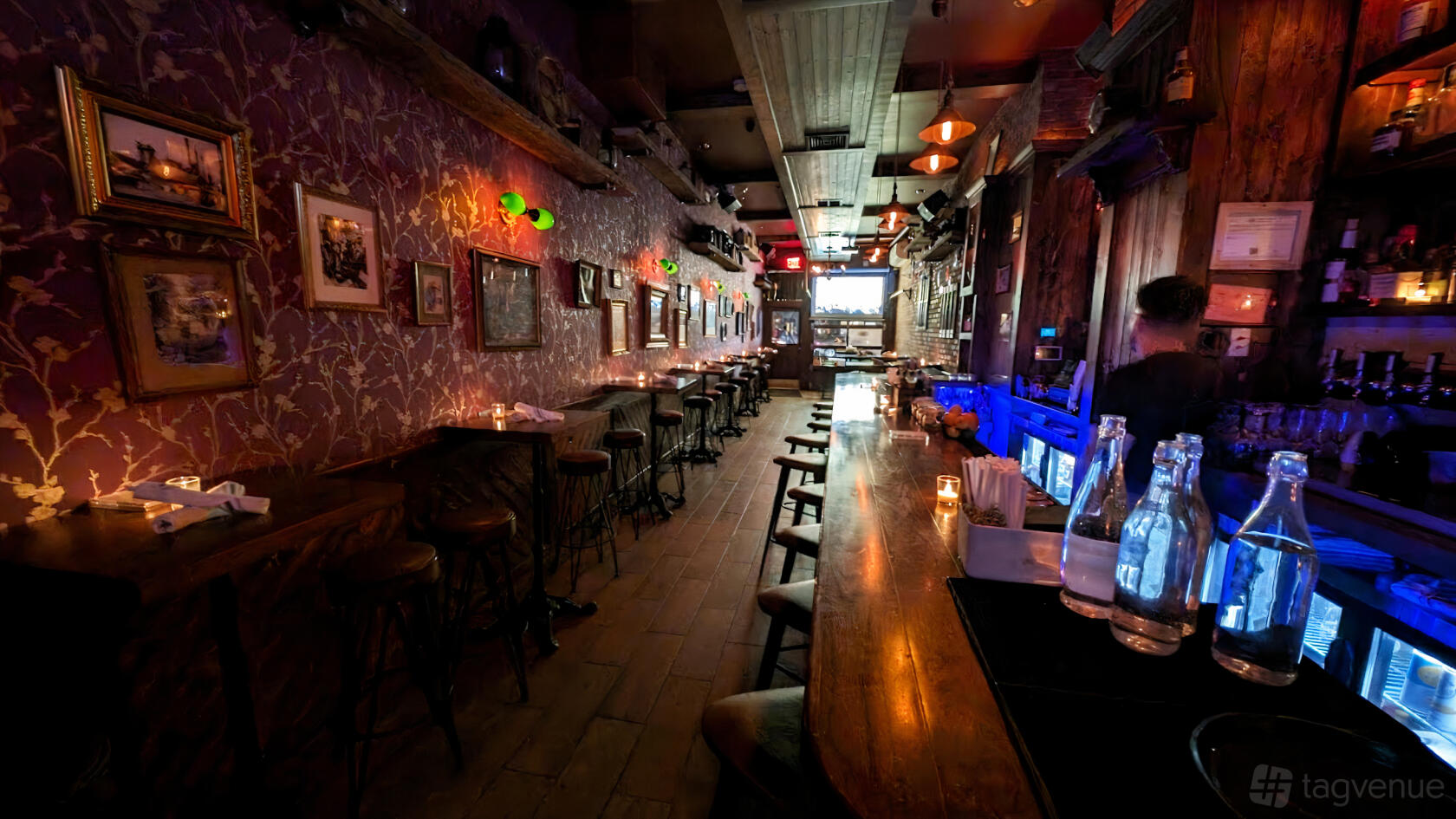 A cocktail bar with patterned wallpaper, candlelit tables, high stools, and a long wooden bar at The Molly Pitcher Club.