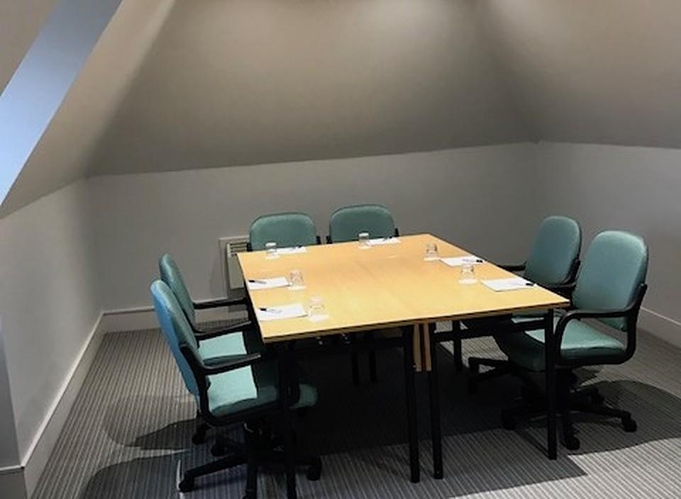 A meeting room with a rectangular wooden table, padded chairs, and notepads set for six at Barnett Hill Hotel.