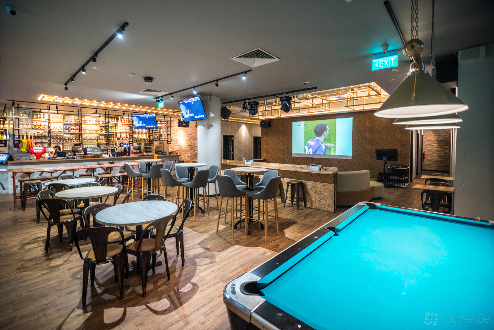 A bar hall with a pool table, round tables with chairs, a projector screen, and a lit bar counter at 7th Heaven KTV Cafe.