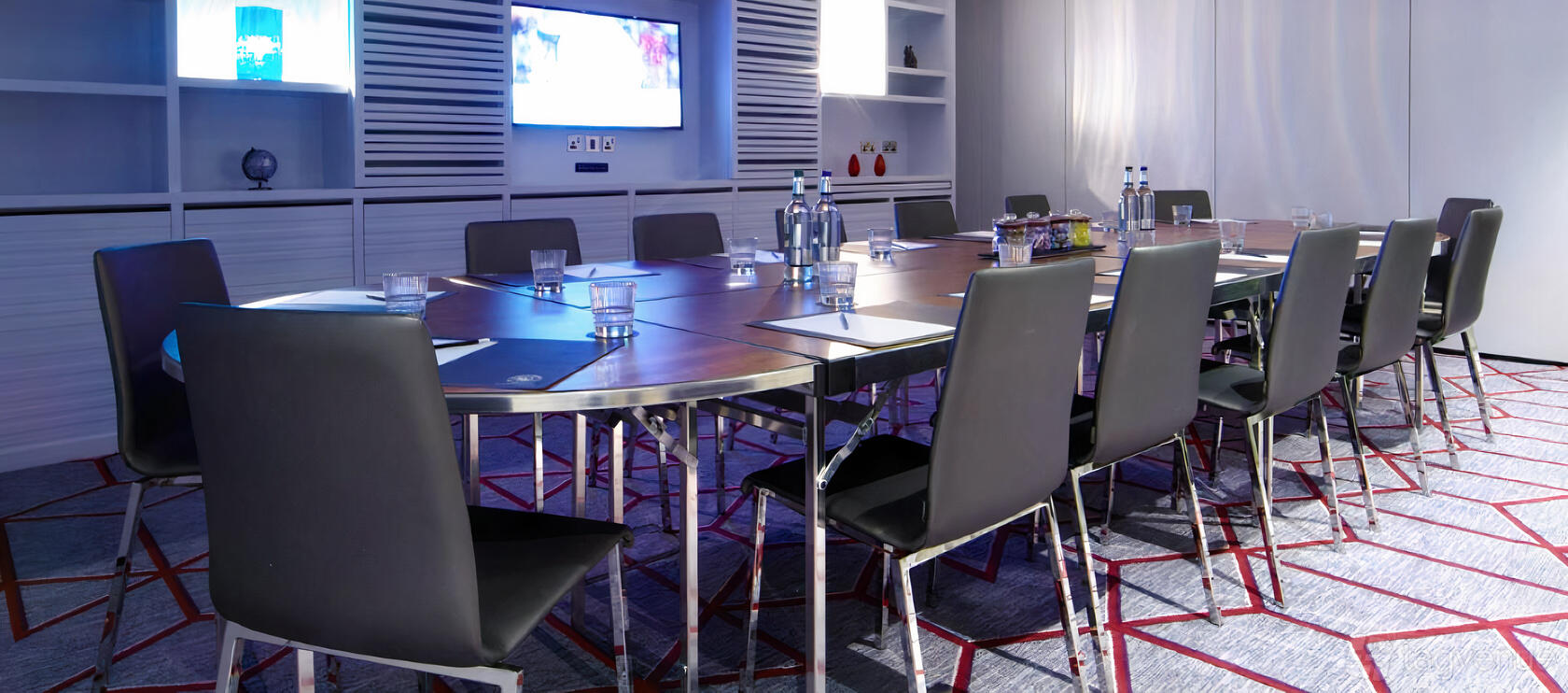 A meeting room with a square conference table, black chairs, bottled water, and notepads at Malmaison Glasgow.