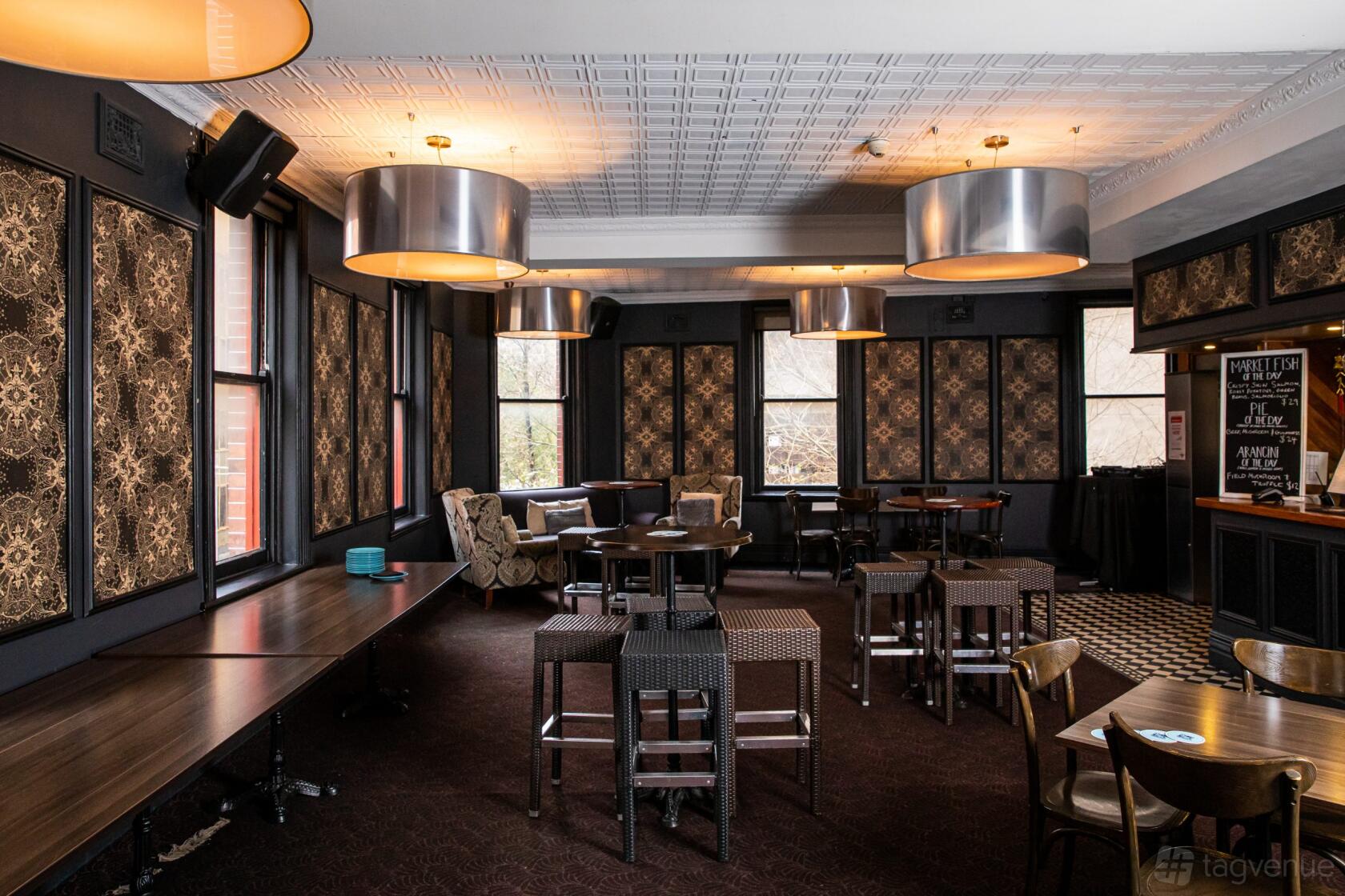 A function room with patterned wallpaper, round pendant lights, and dark wood tables at The Belvedere Hotel.
