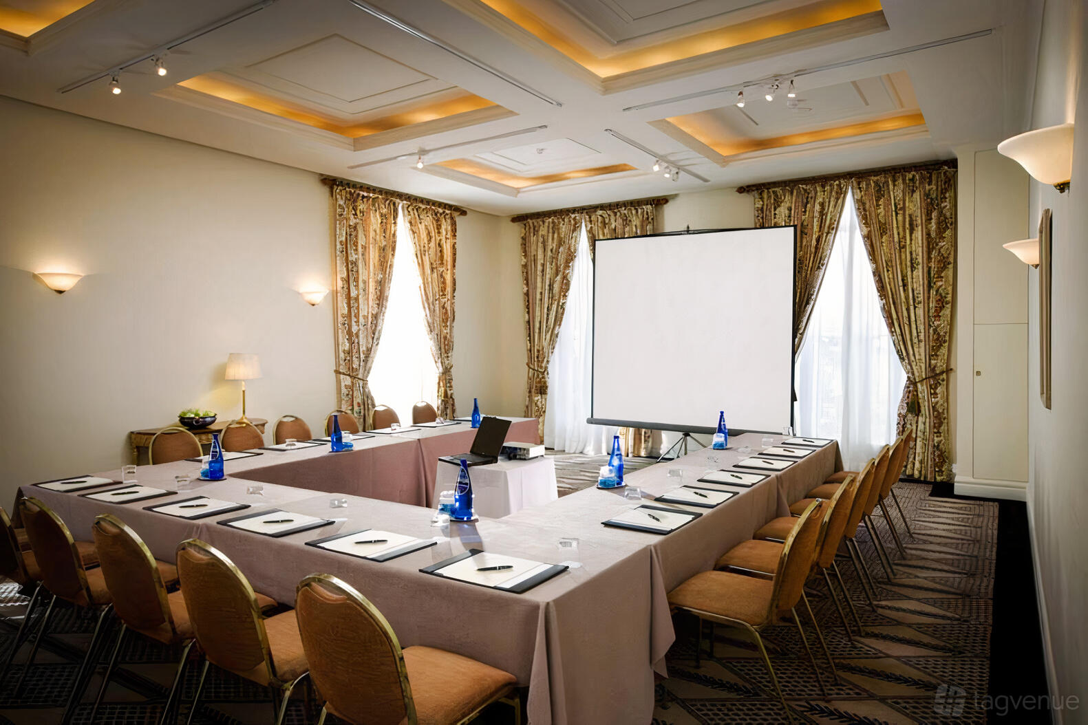 A meeting room with U-shaped tables, gold chairs, large windows with drapes, and a projector screen at Lilianfels Resort & Spa.