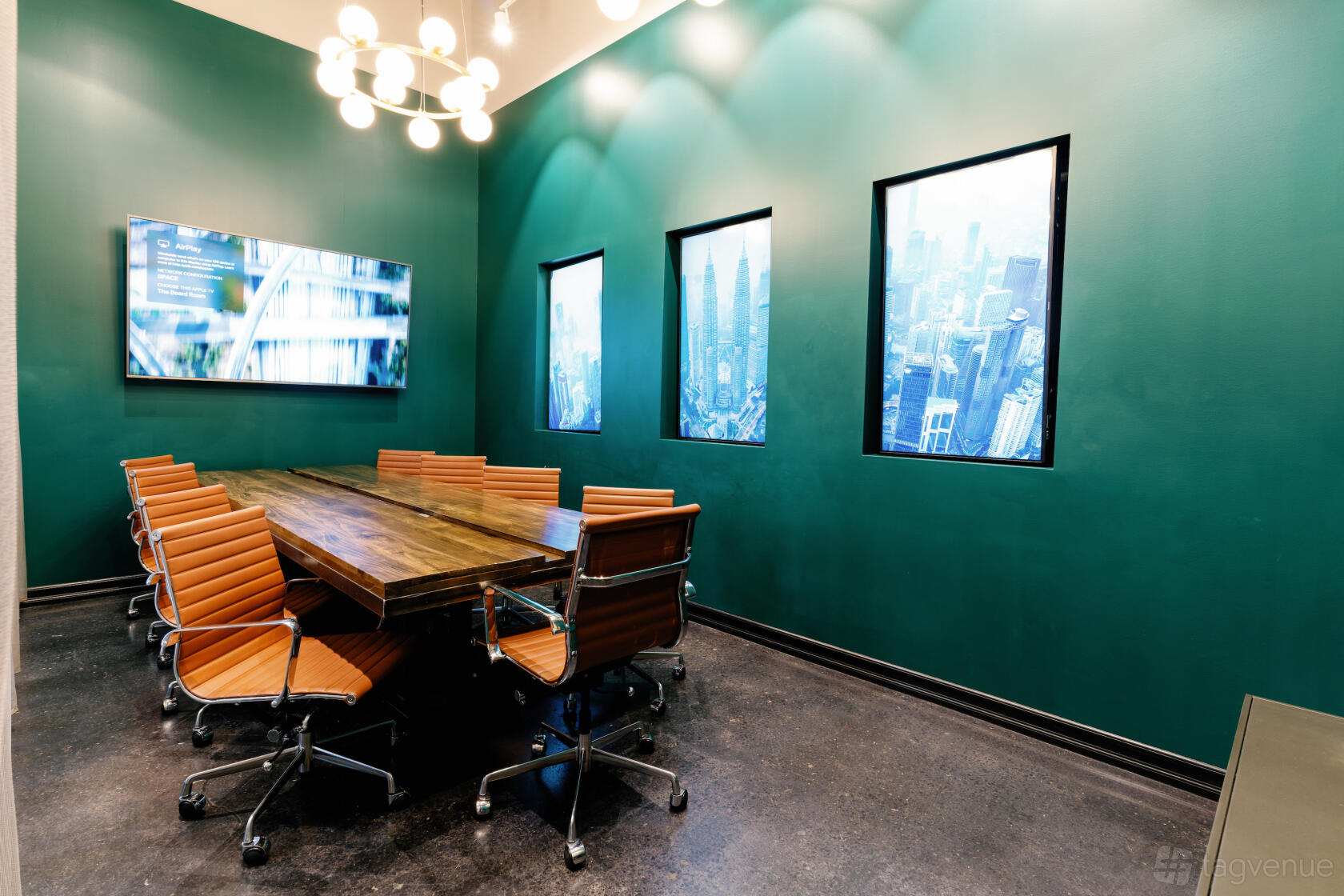 A meeting room with a wooden conference table, leather chairs, wall-mounted screen, and tall windows at Corporate CoWork.