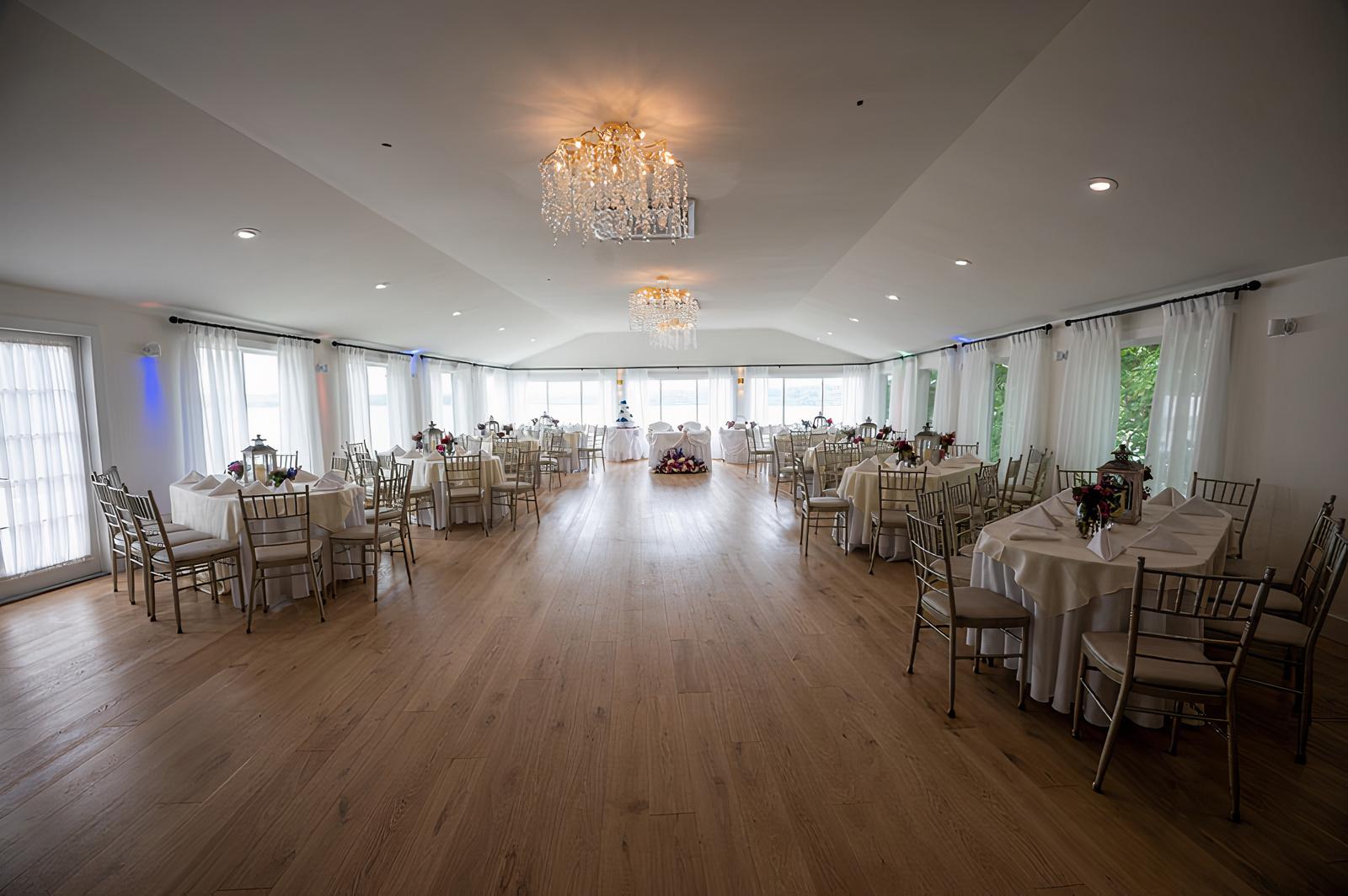 An event venue with wood floors, chandeliers, and round tables with white linens at Beach Club Estate.