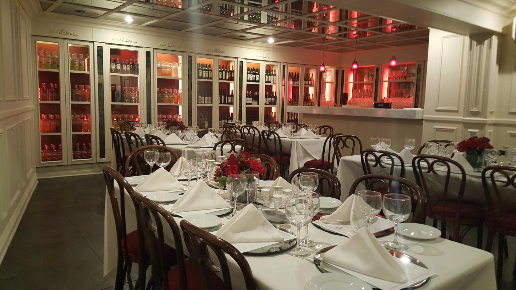 A restaurant private room with white tablecloths, glassware, wooden chairs, and wall-to-wall wine displays at Prime Bistro.