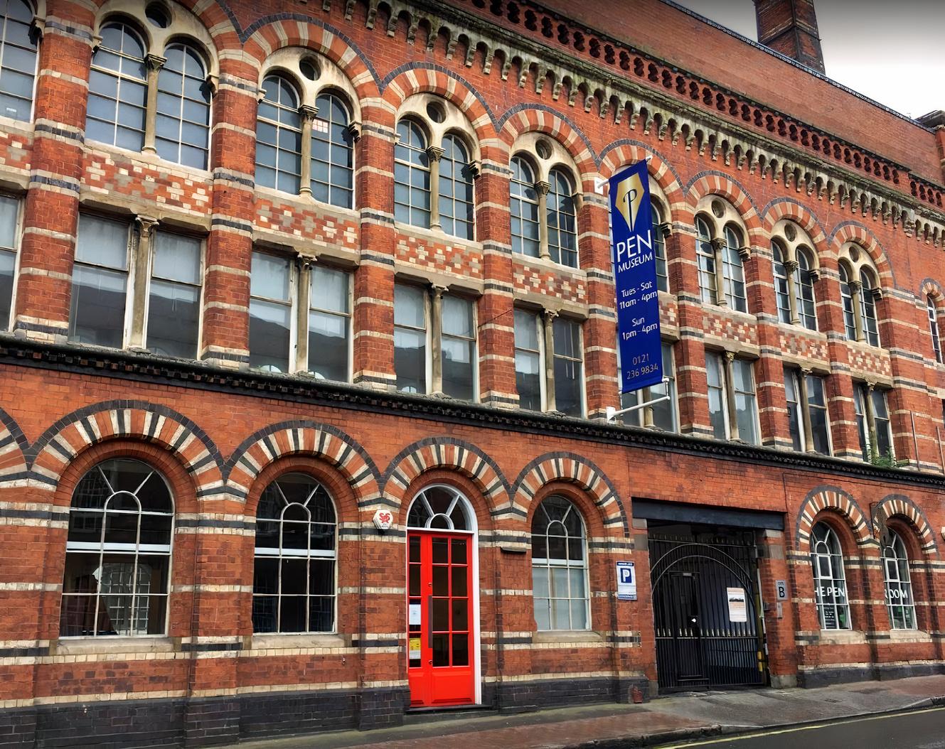 A museum with a red brick Victorian facade, arched windows, and a blue sign at The Pen Museum.