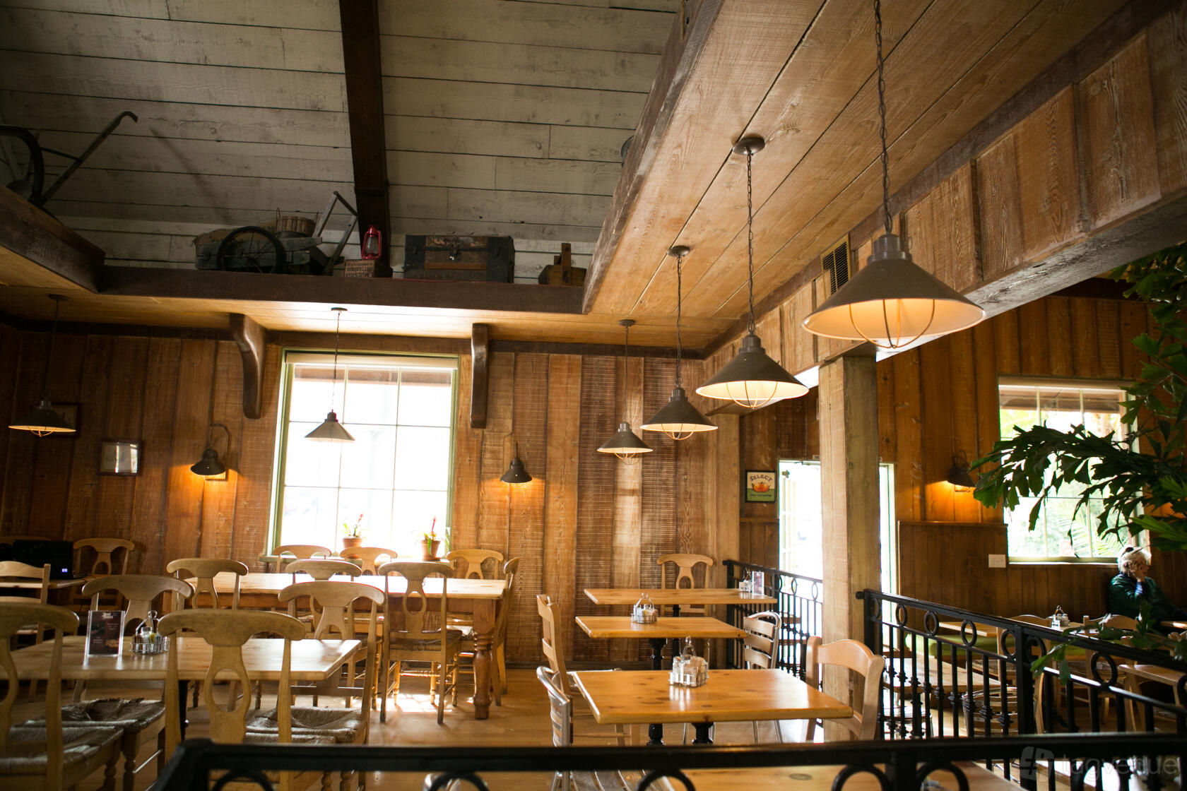 A restaurant dining area with wooden walls, exposed beams, large windows, and hanging pendant lights at Coral Tree Cafe - Encino.