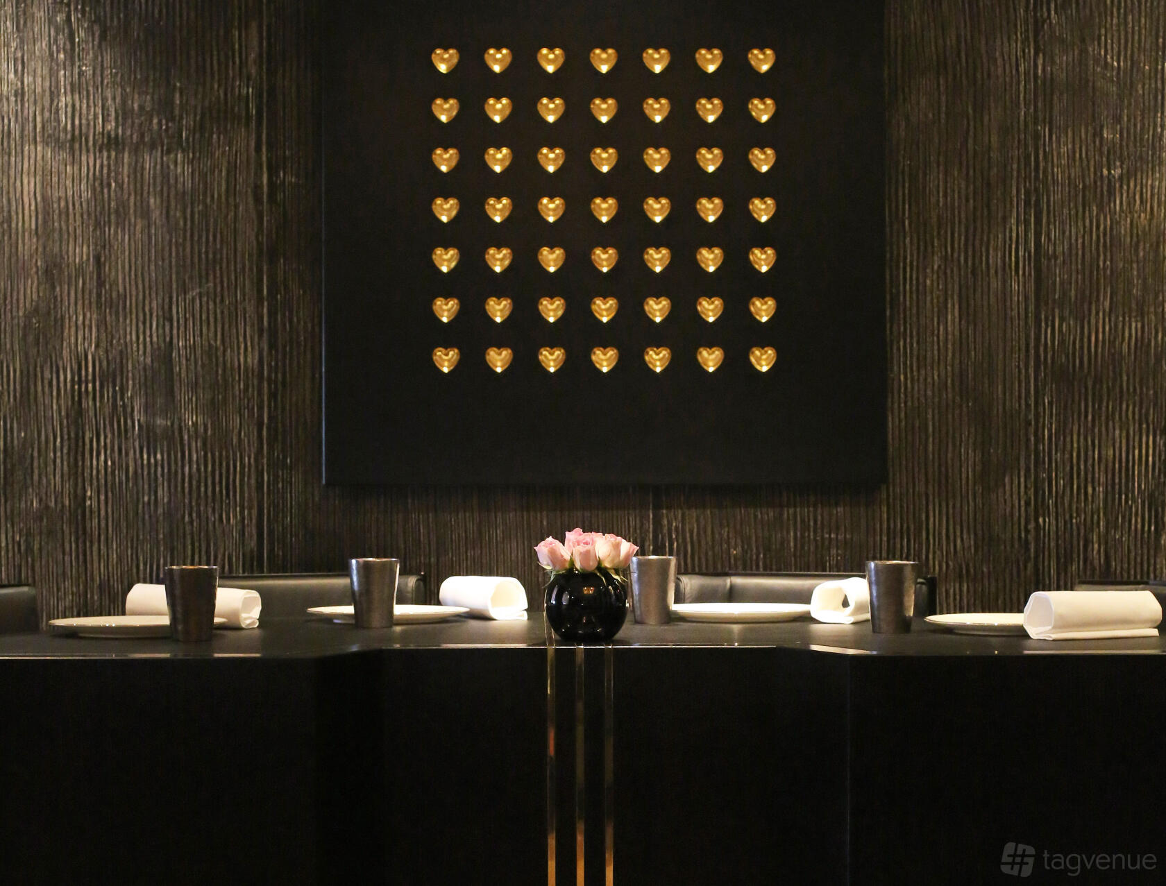 A restaurant dining room with a black table, pink flower centerpiece, and gold heart wall art at Restaurant Gordon Ramsay.