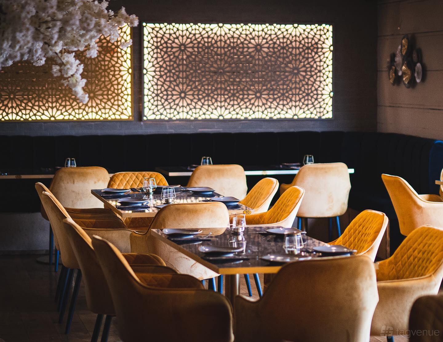 An event space with patterned wall panels, velvet banquette seating, and tables set with plates and glasses at Haveli The Yard.