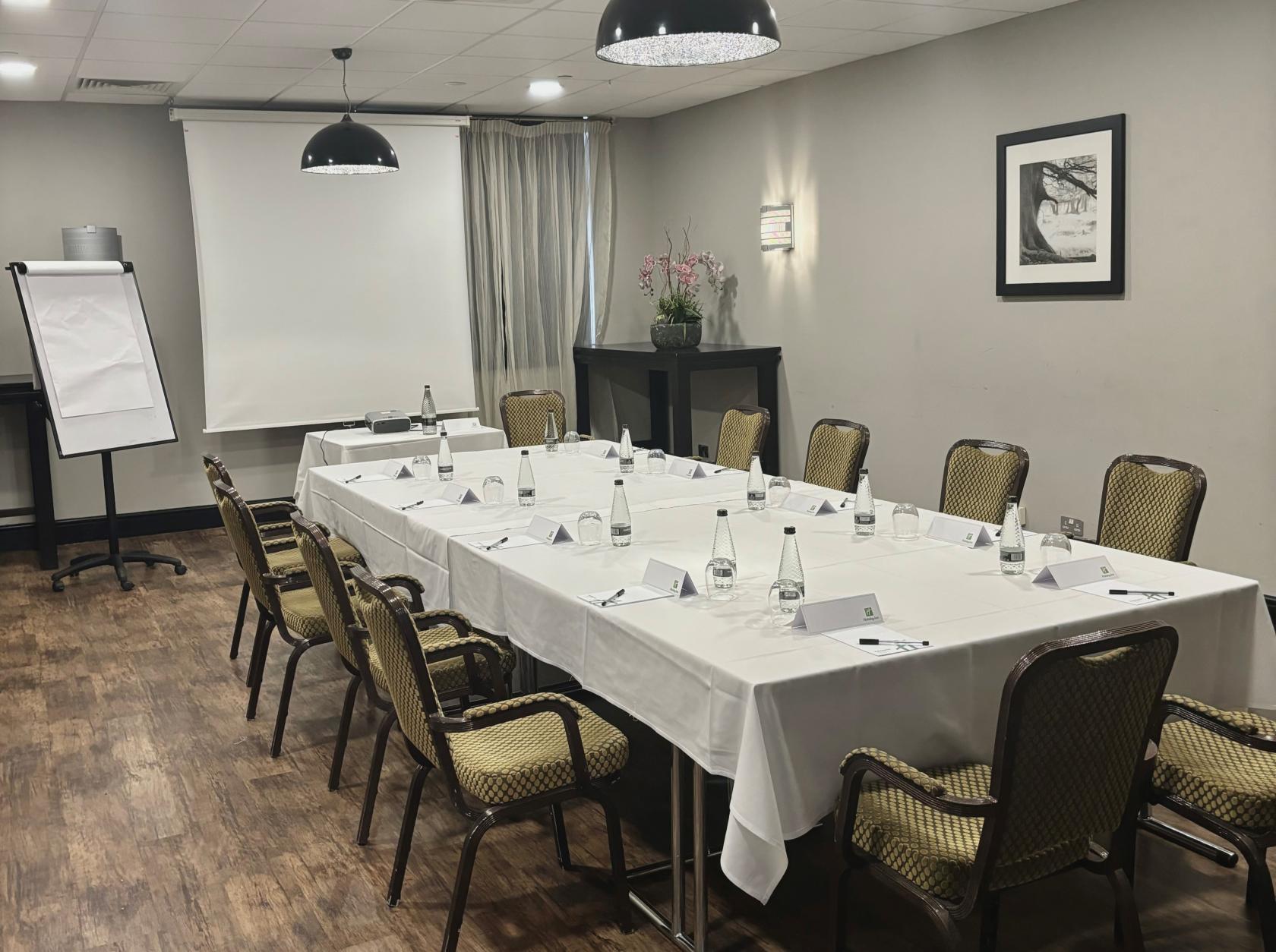 An event space with a U-shaped table setup, white linens, and presentation screen at Holiday Inn Kenilworth-Warwick.