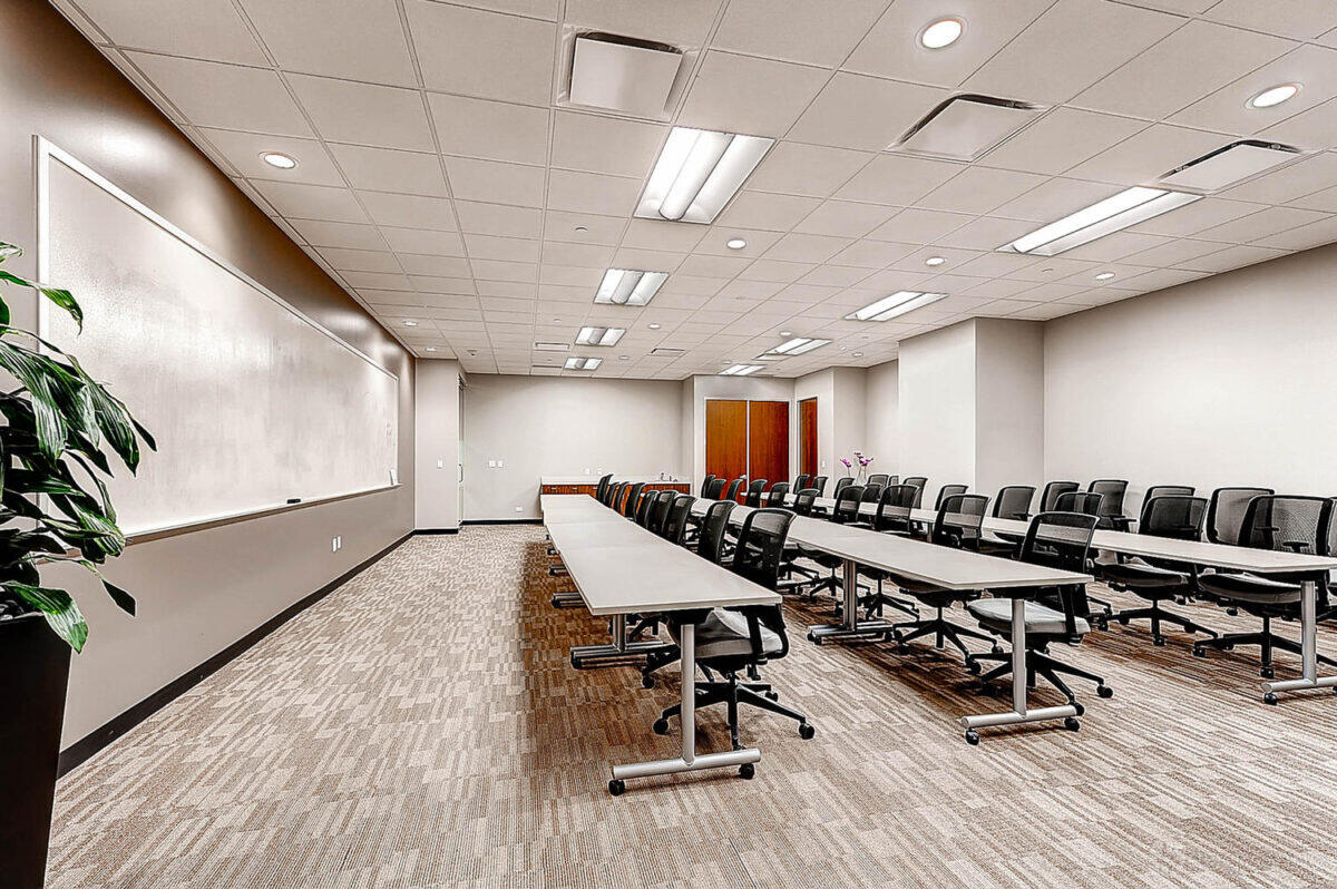 A classroom with long tables, black office chairs, a large whiteboard, and overhead fluorescent lights at Coalition Space Denver.