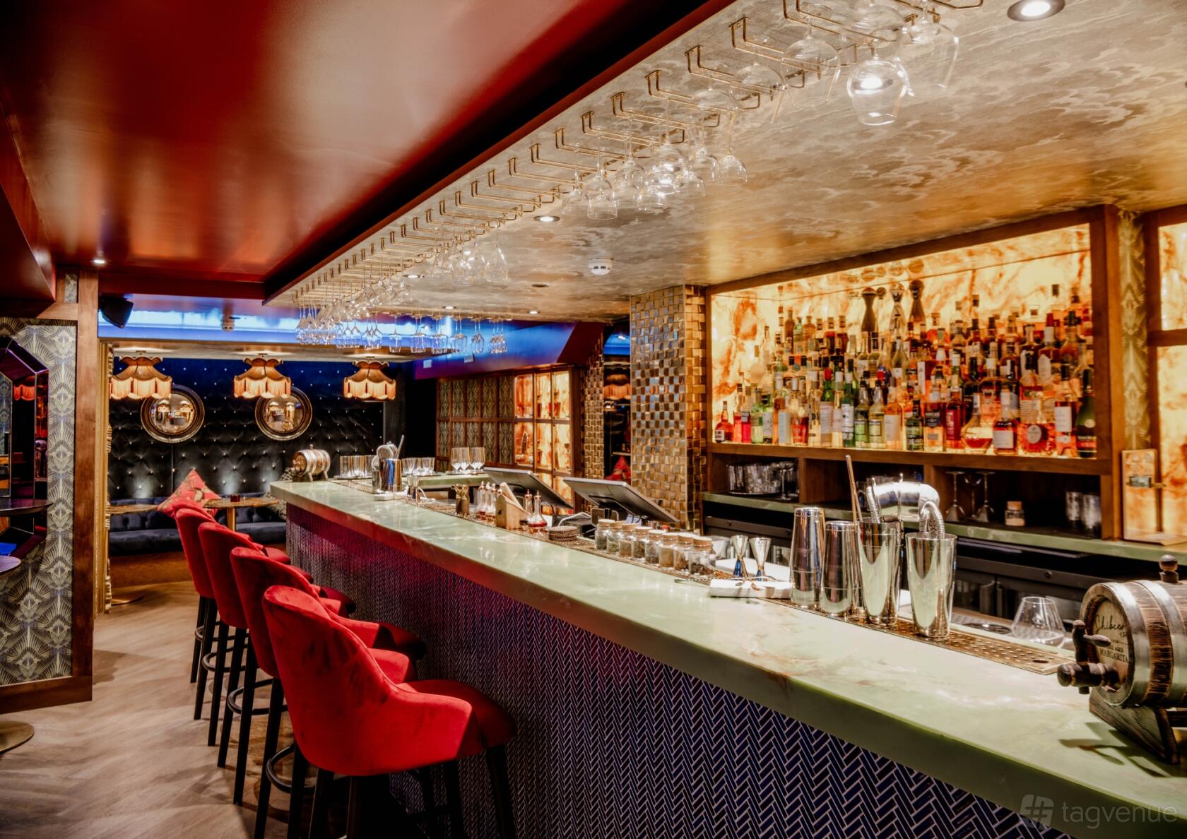 A cocktail bar with a green marble counter, red velvet barstools, and illuminated bottle display at BÓHA London.