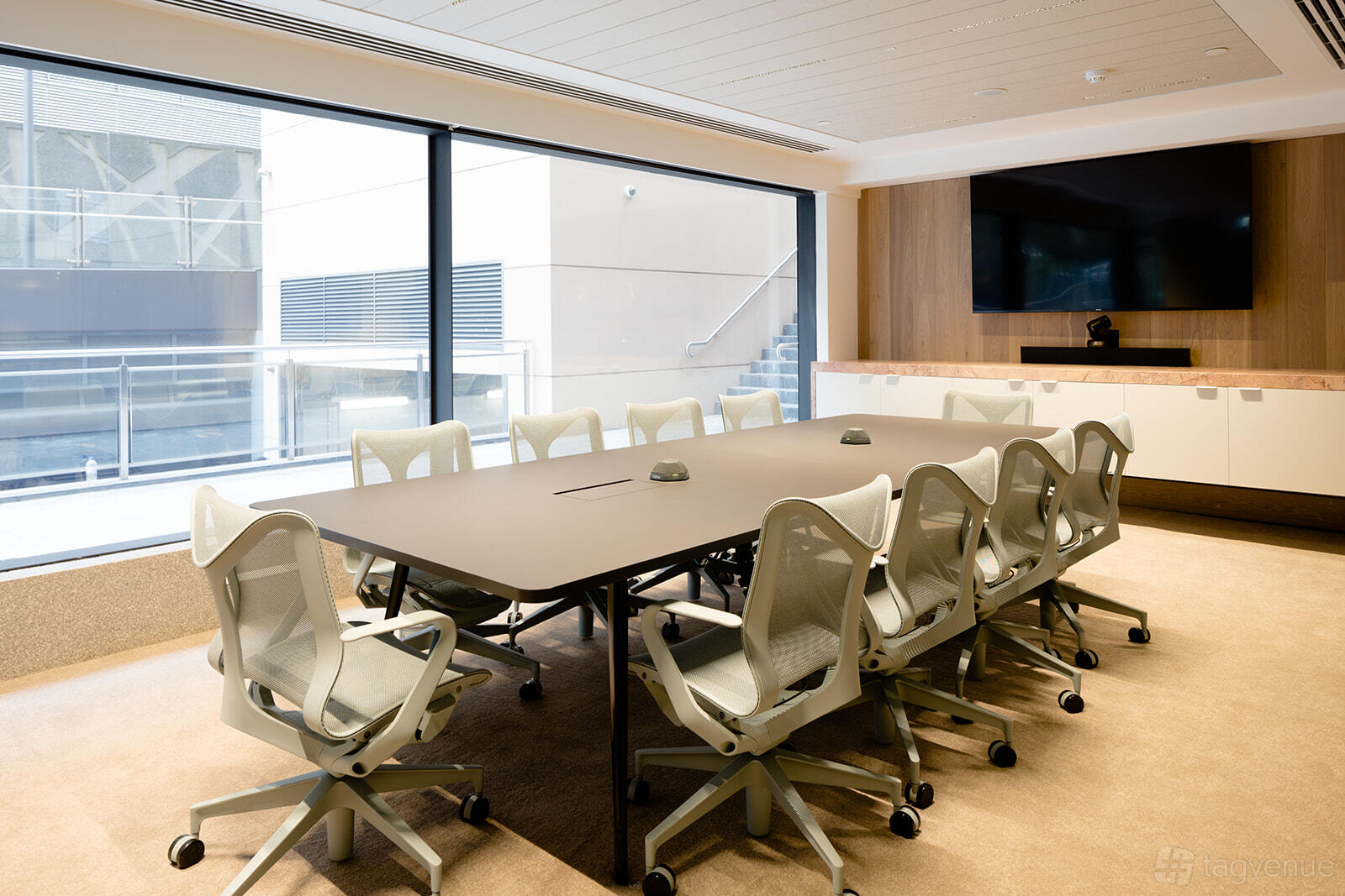 A meeting room with a long conference table, ergonomic chairs, large windows, and a wall-mounted screen at Centred.