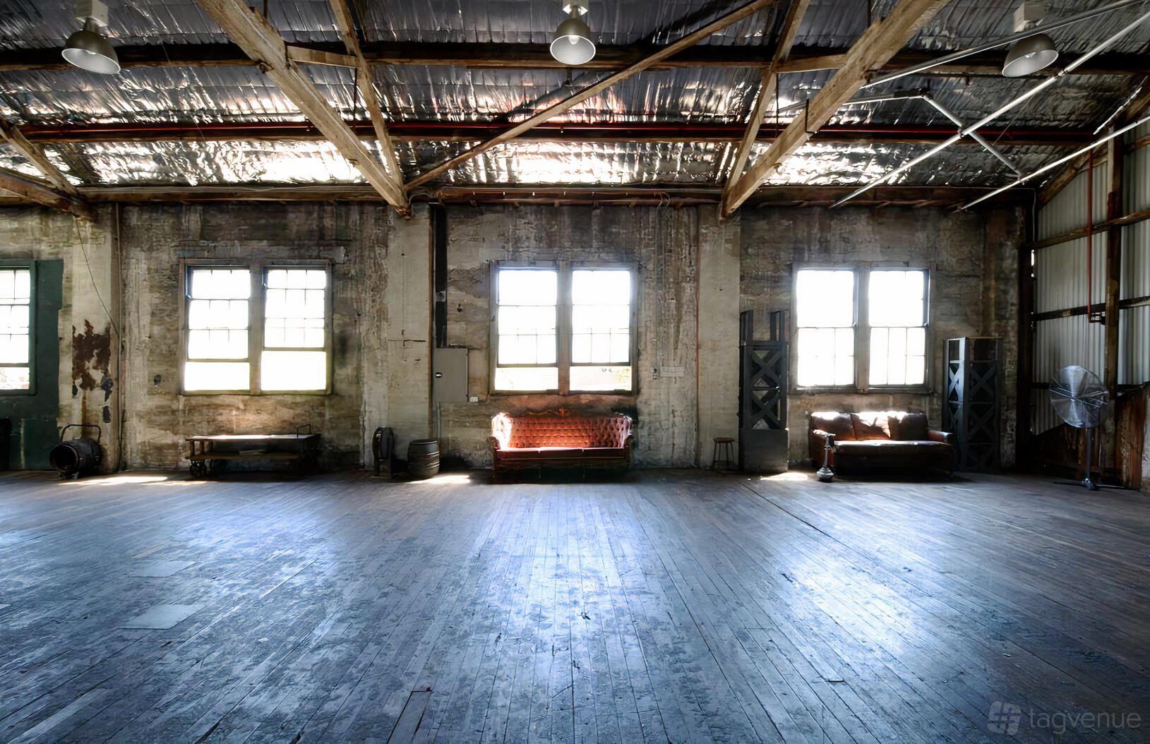 A warehouse space with exposed beams, large industrial windows, and vintage sofas at Sydney Props Photo Studios.