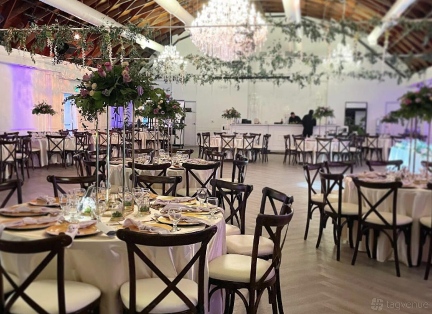 A ballroom with round tables set with floral centerpieces, cross-back chairs, and chandeliers at VASA.