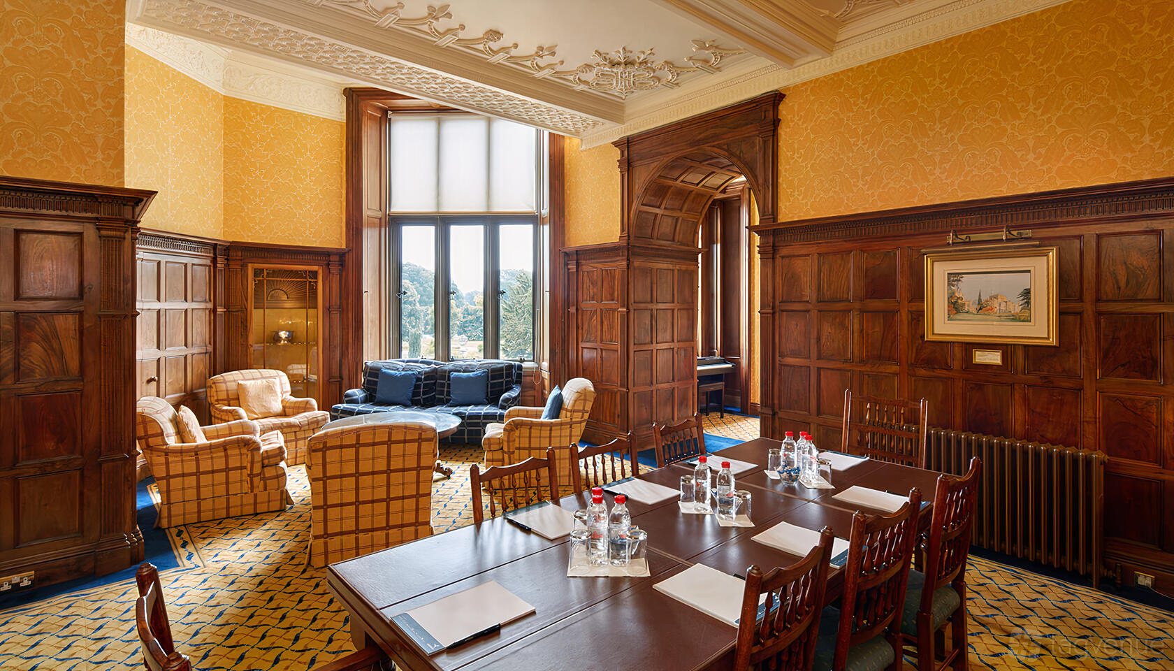 A castle sitting room with large arched windows, wood paneling, and armchairs at Ashridge House.