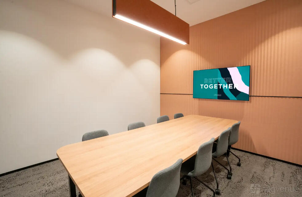 A meeting room with a long wooden table, grey chairs, wall-mounted screen, and pendant lighting at Waterman at Eastland.