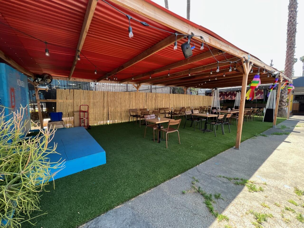 An outdoor restaurant patio with red canopy, string lights, artificial turf, and wooden tables at Kombu Sushi Silver Lake.