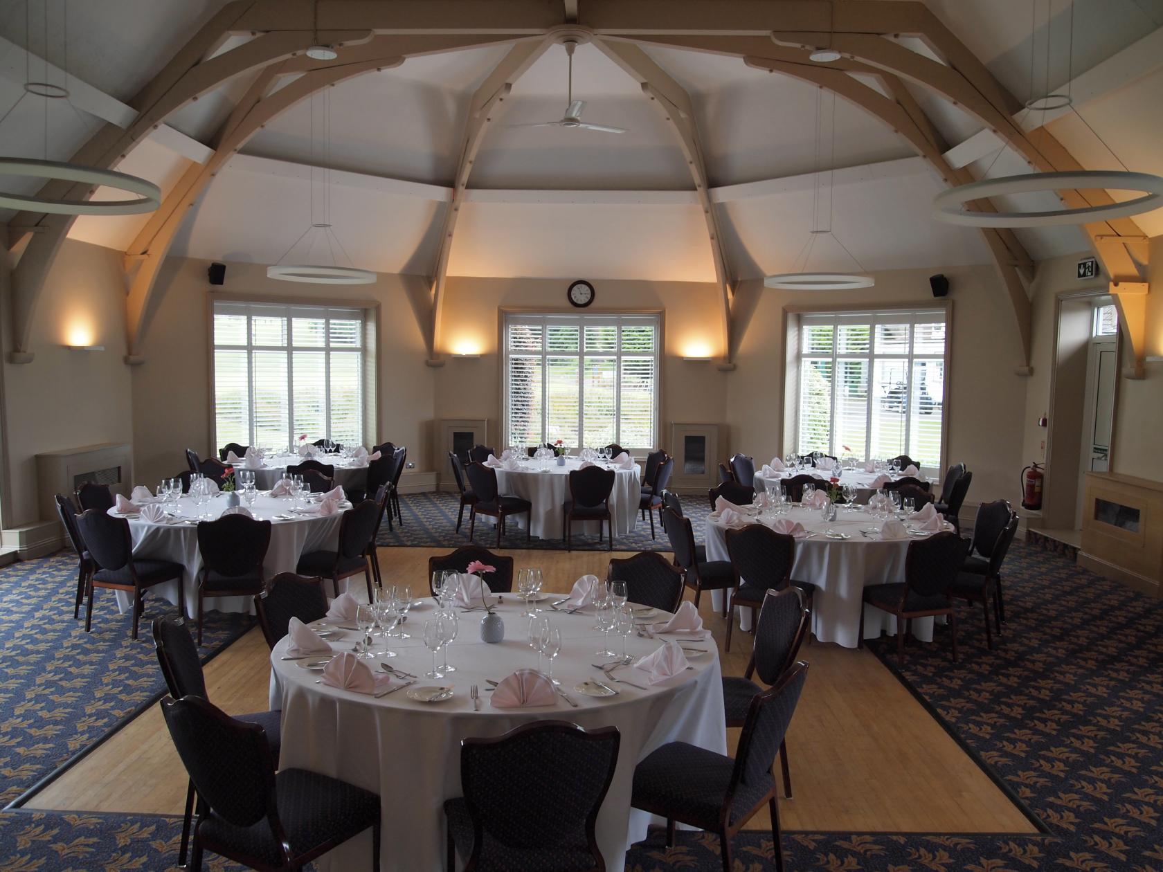 A function room with round tables dressed in white linens and vaulted wooden beams at Shirley Park Golf Club.