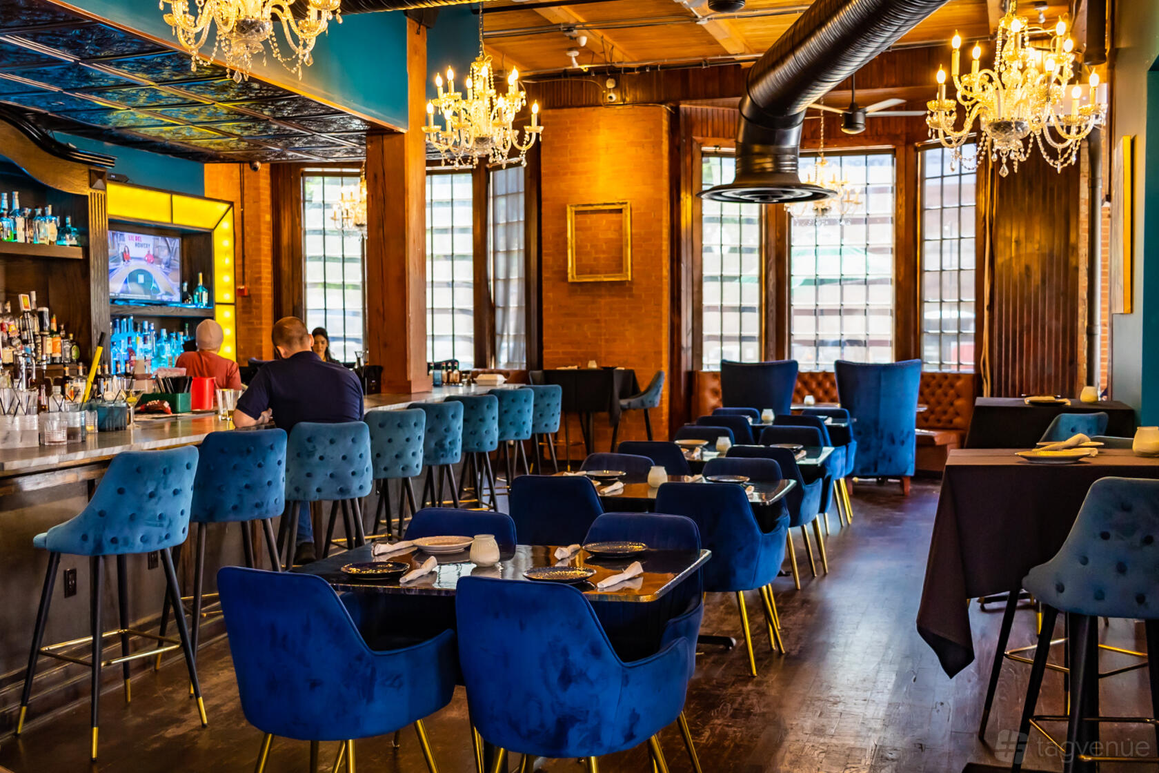 An event space in a restaurant with blue velvet chairs, chandeliers, and a marble bar at Chet's.