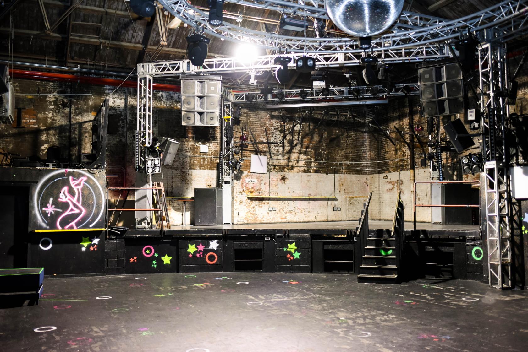 A basement nightclub with exposed brick walls, a large dance floor, stage, neon accents, and disco ball at 3 Dollar Bill.