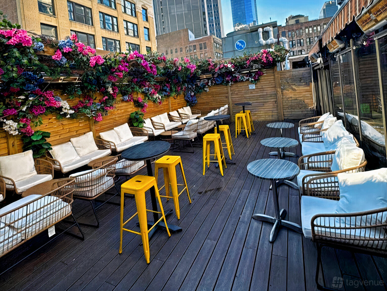 A rooftop bar with wooden decking, yellow stools, cushioned seating, and overhead floral decor at k-32 Rooftop Bar.