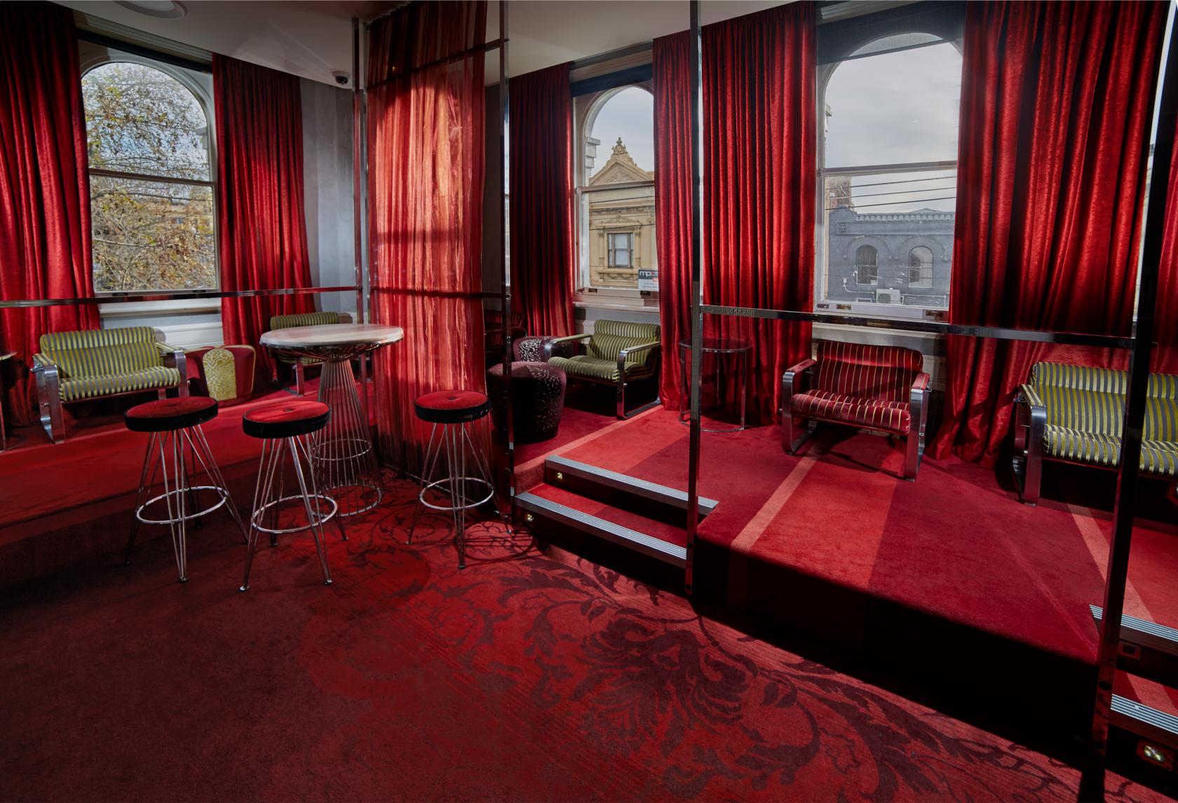 A pub lounge with red velvet curtains, patterned carpet, arched windows, and mixed seating at Temperance Hotel.