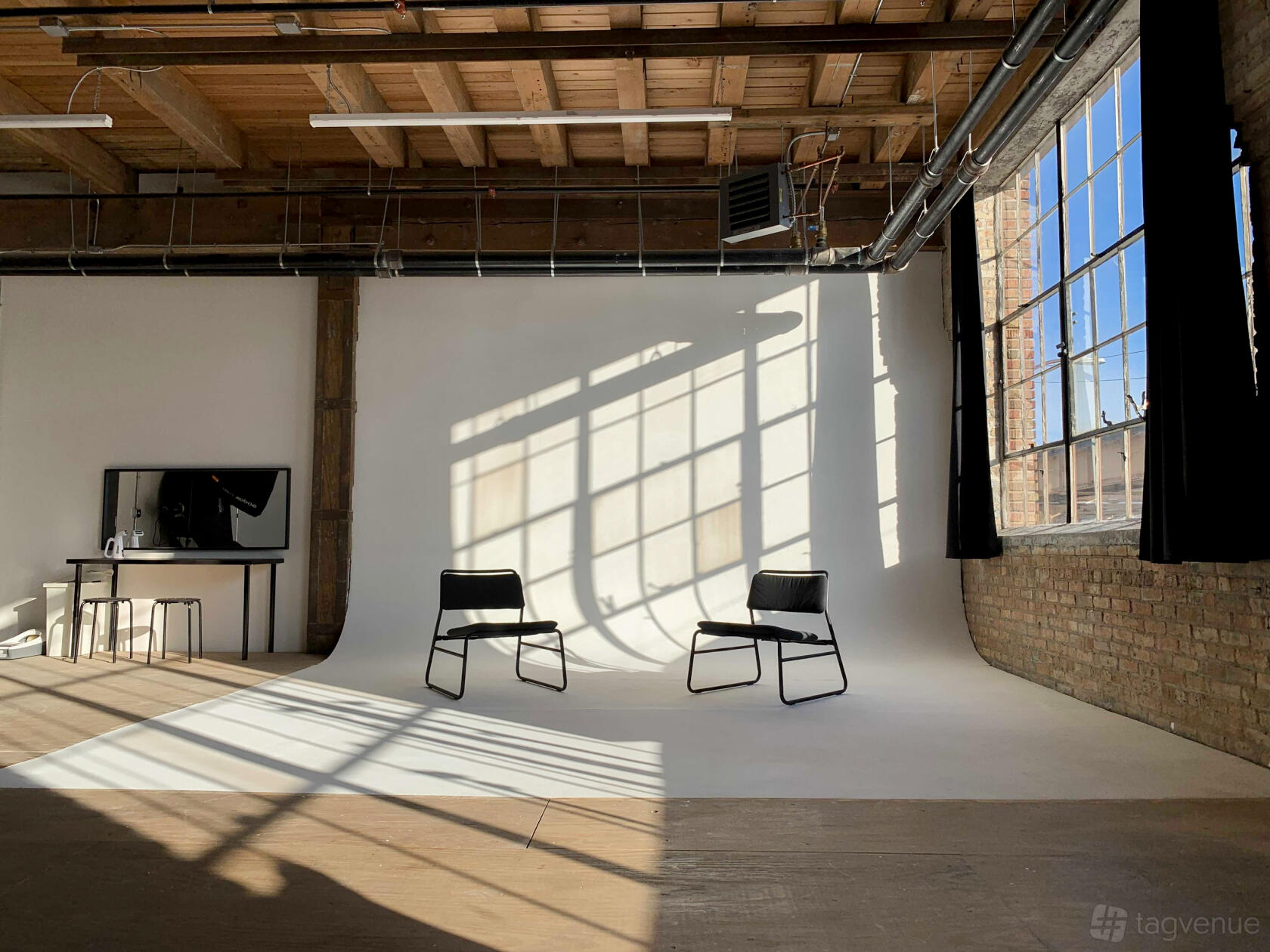 A photo studio with a white cyclorama wall, two black chairs, exposed brick, and large industrial windows at MikSpace Chicago.