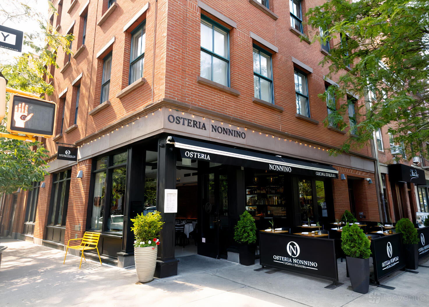 A corner restaurant with outdoor seating, large windows, and black awnings at Osteria Nonnino.