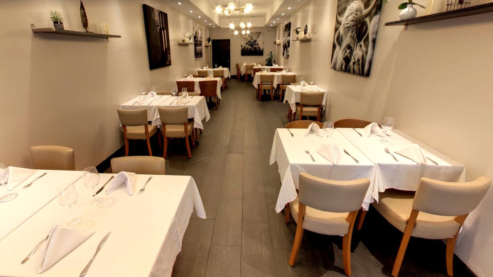 A dining room with white tablecloths, beige chairs, wall art, and overhead lighting at The Harbour Grill.