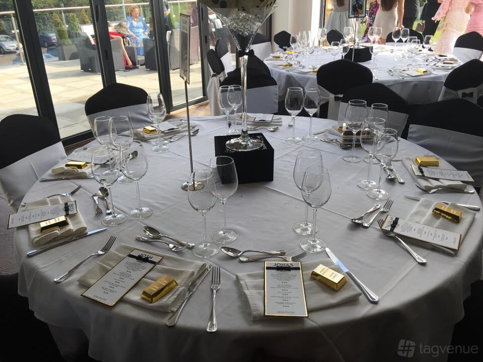 An event venue with round tables set with glassware, menus, and gold-wrapped favors at The Willows.