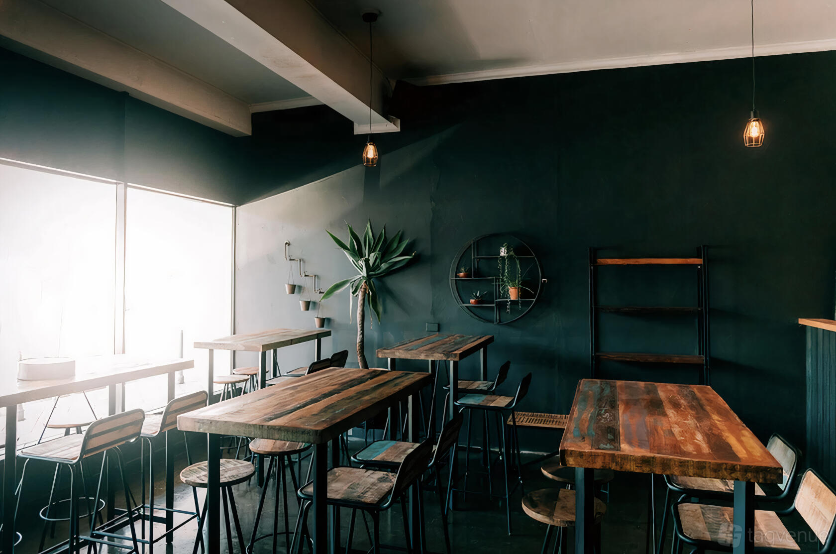 A pub with rustic wooden tables, metal stools, pendant lighting, and dark walls at Twang Brewing.