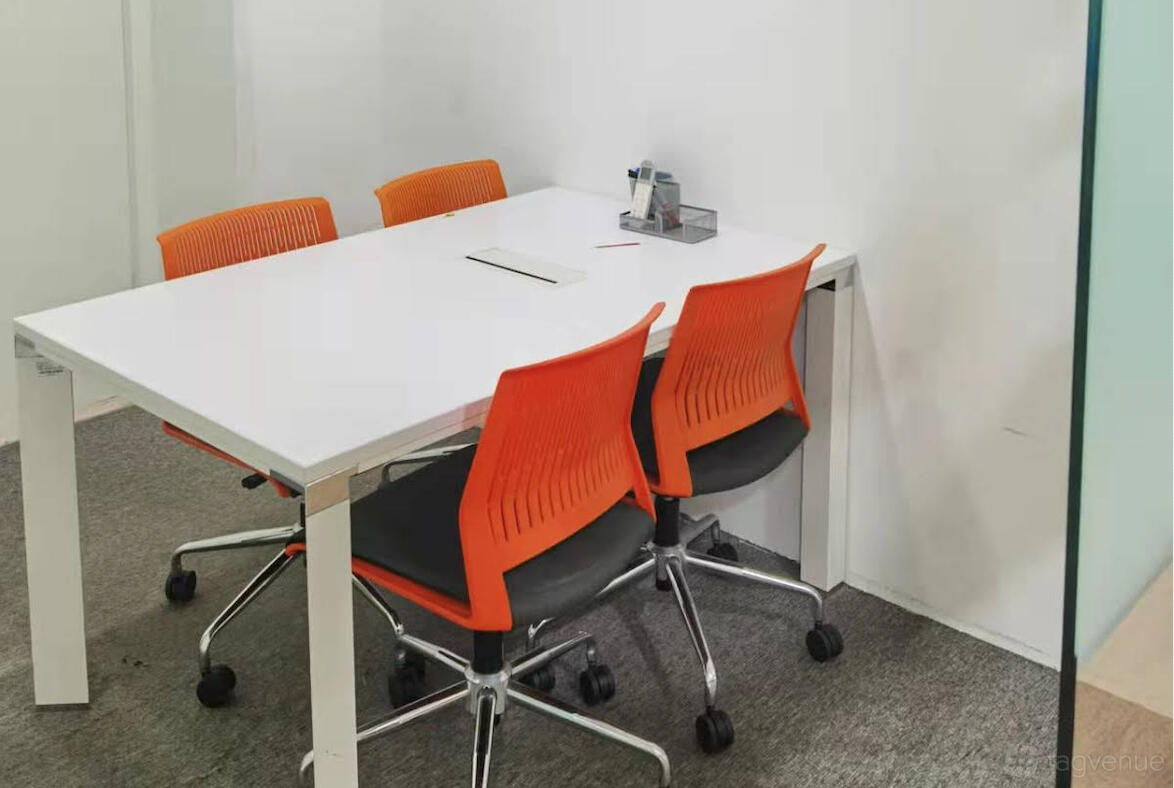 A meeting room with a white table, bright orange chairs, and carpeted flooring at UClub Singapore OneNorth.