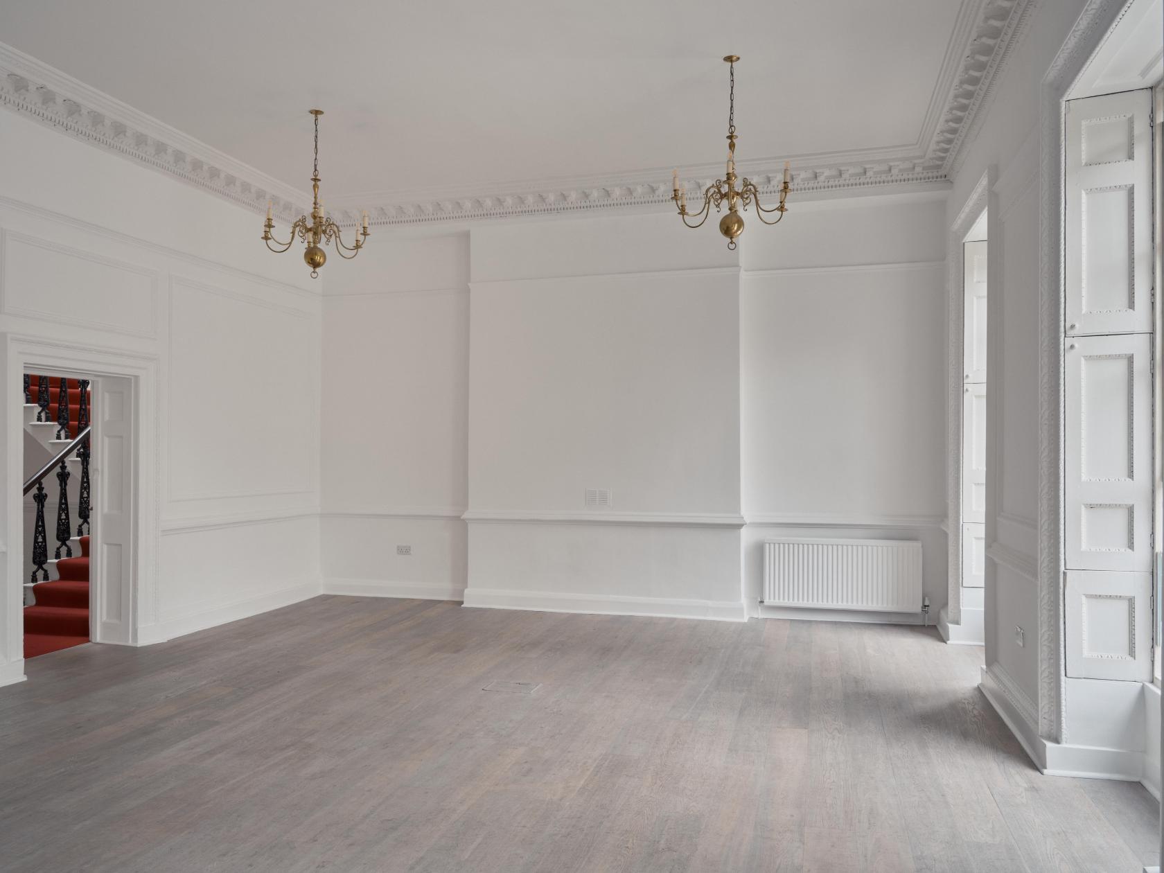 An event space with white paneled walls, chandeliers, and large windows in the Music Room at Pushkin House.
