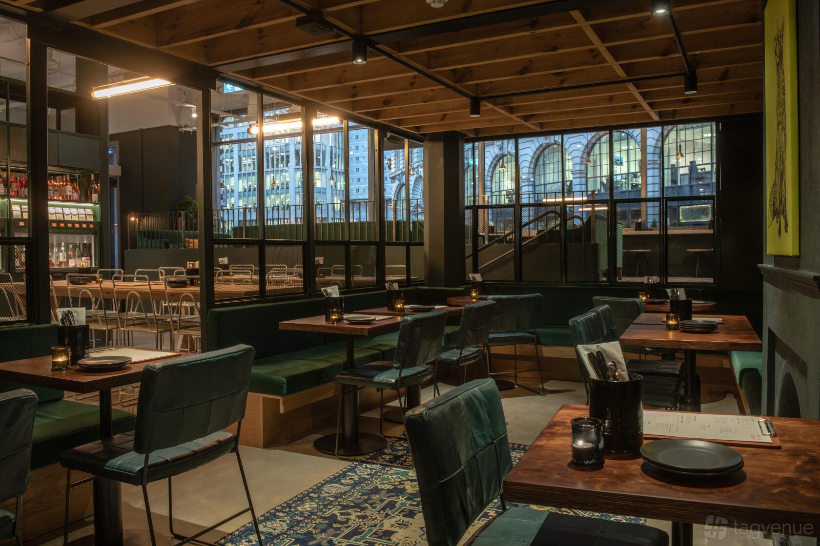 An event space in a bar with wooden tables, velvet chairs, soft lighting, and large windows at Vagabond Monument.