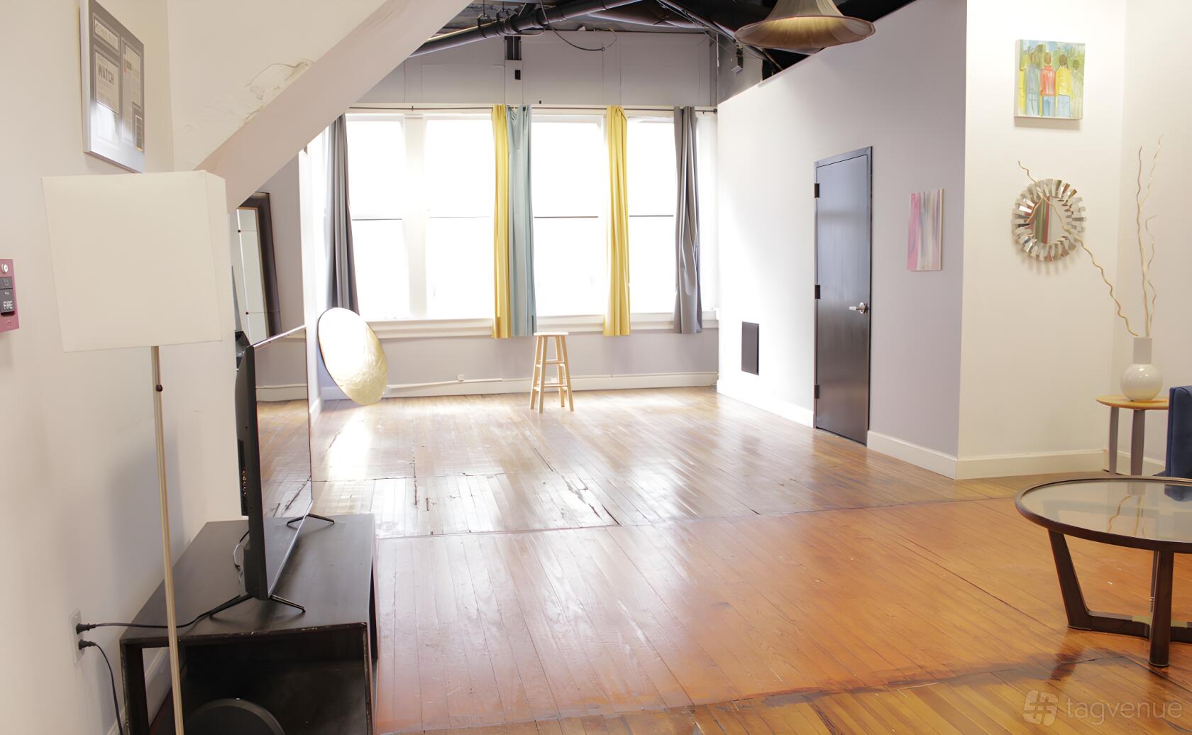 An event space with hardwood floors, large windows with multicolored curtains, and exposed ceiling beams at The Vault Atlanta.