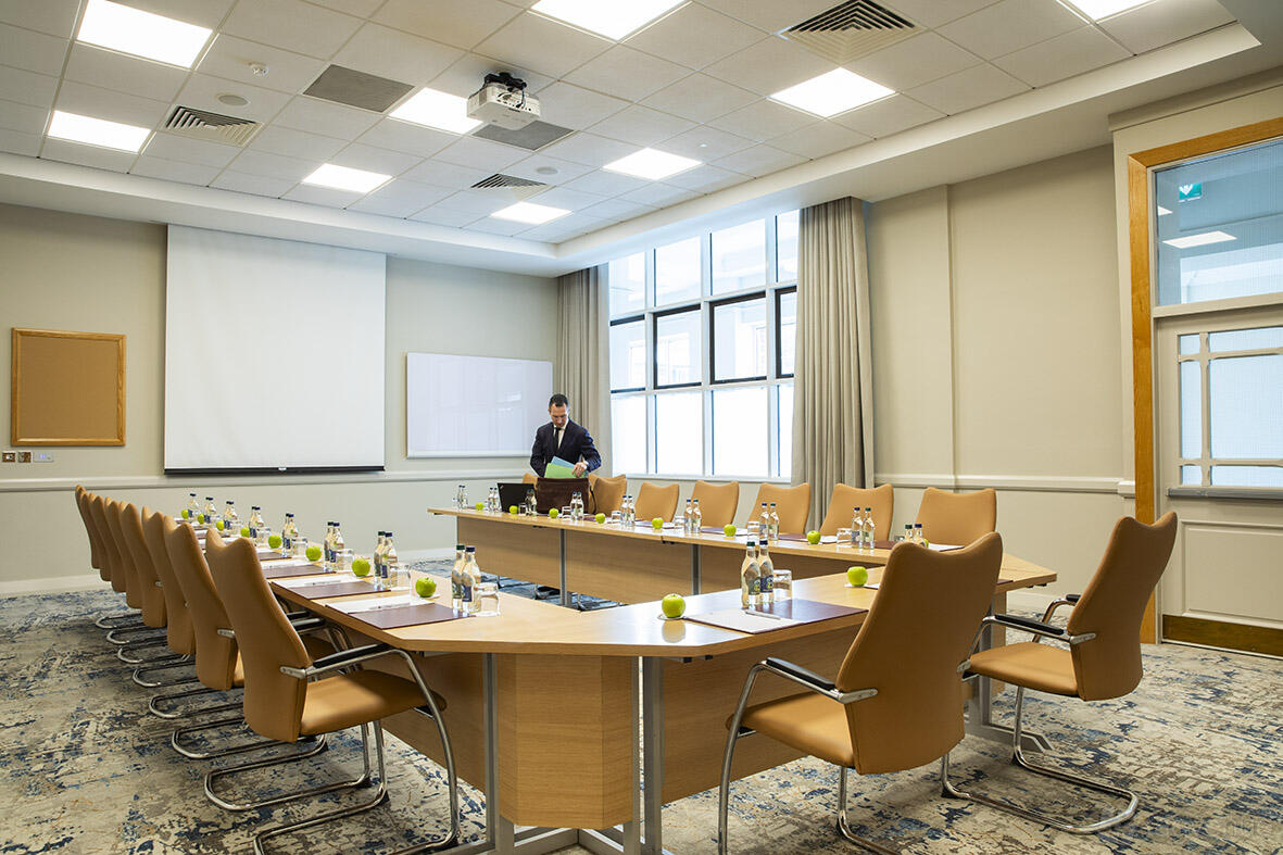 A meeting room with U-shaped conference tables, ergonomic leather chairs, and a projector screen at Grand Hotel.
