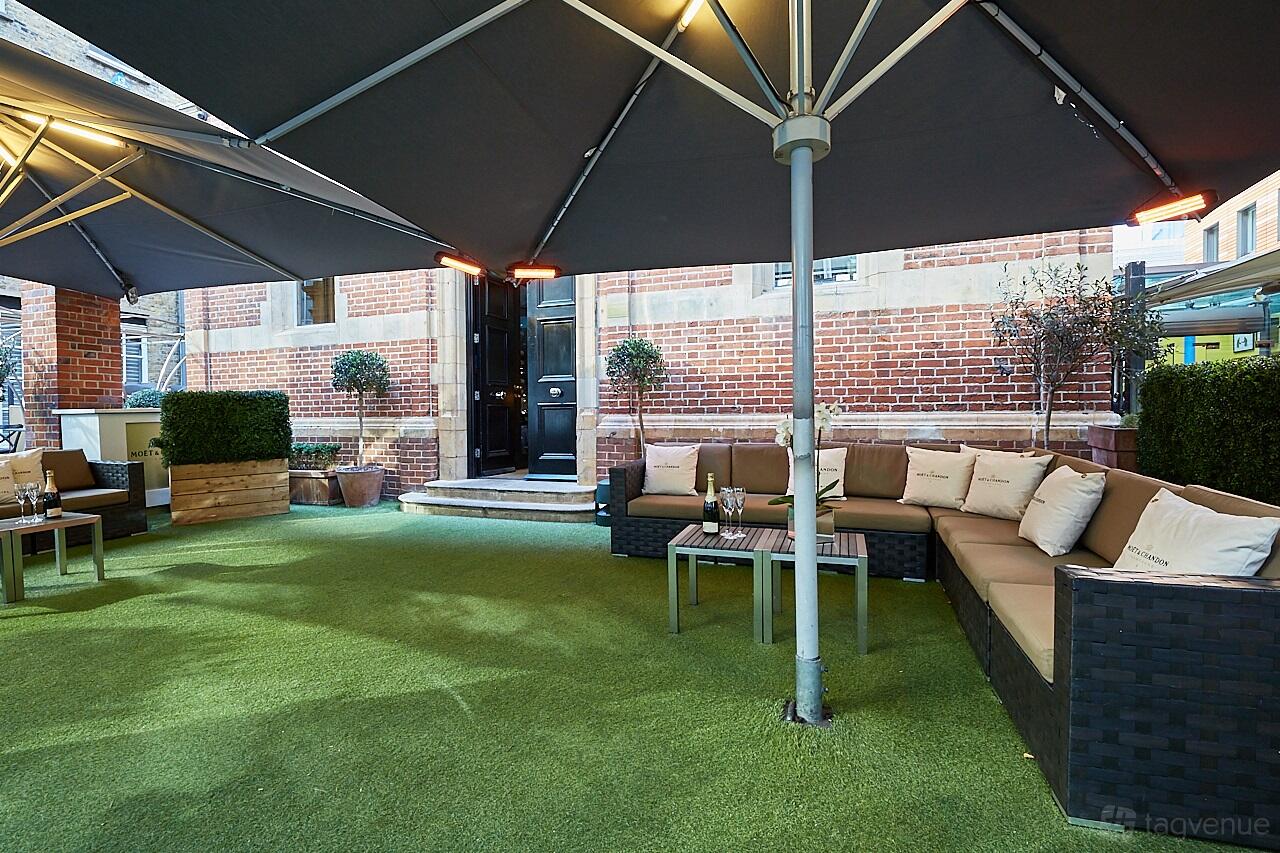 A restaurant garden with wicker sofas, green artificial turf, and large umbrellas at Galvin La Chapelle.