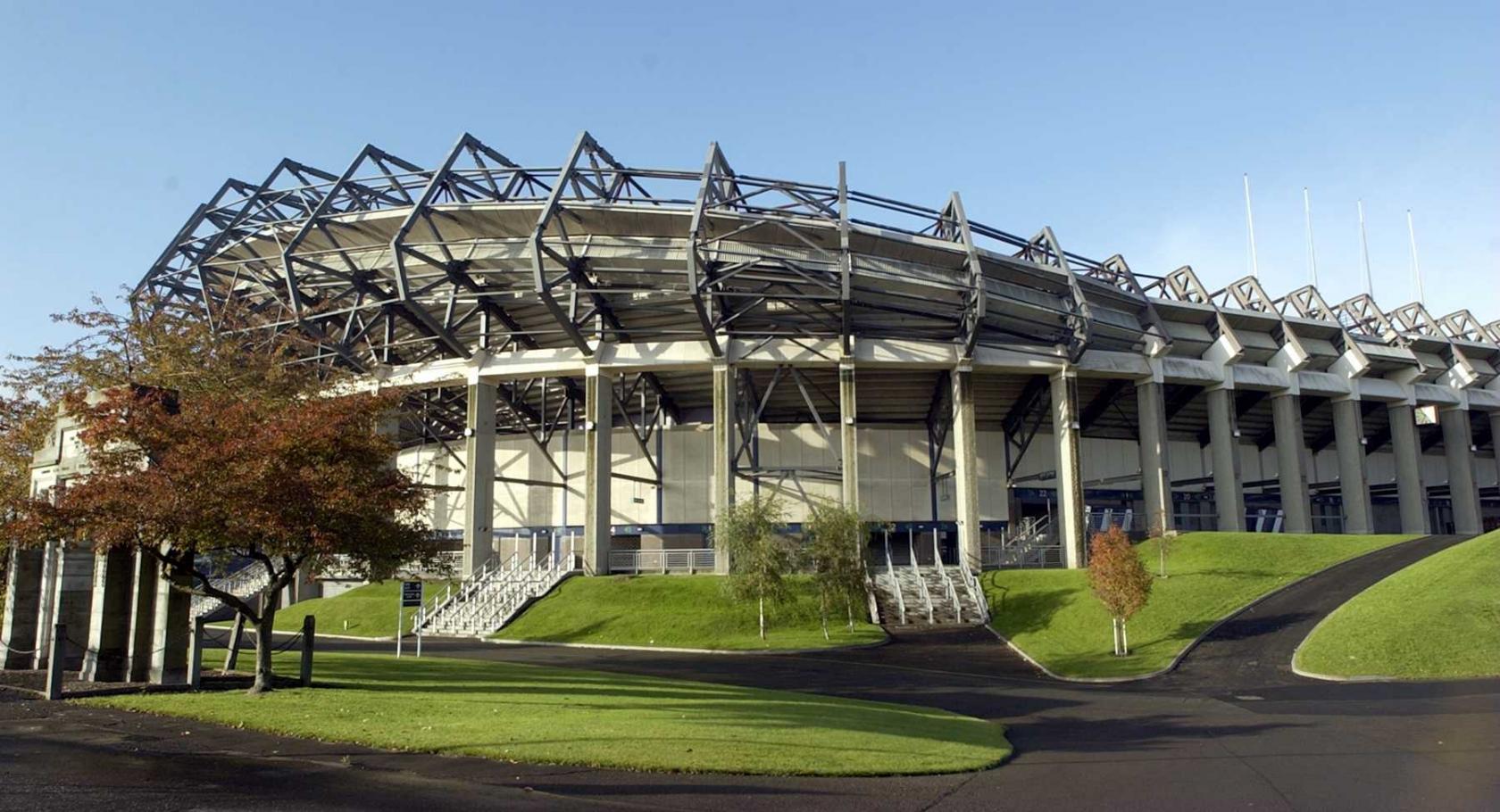 A stadium with tiered seating, exposed steel framework, and landscaped pathways at BT Murrayfield Stadium.