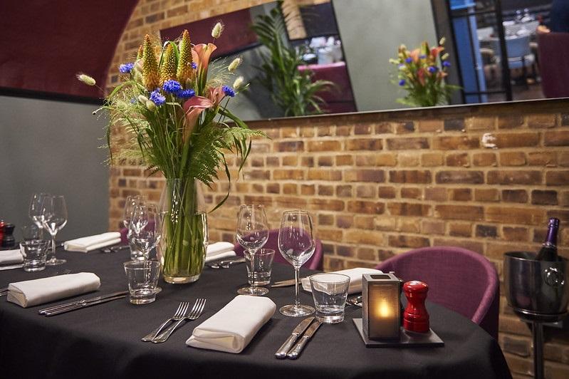 A meeting room with exposed brick walls, black tablecloths, and floral centerpieces at Malmaison London